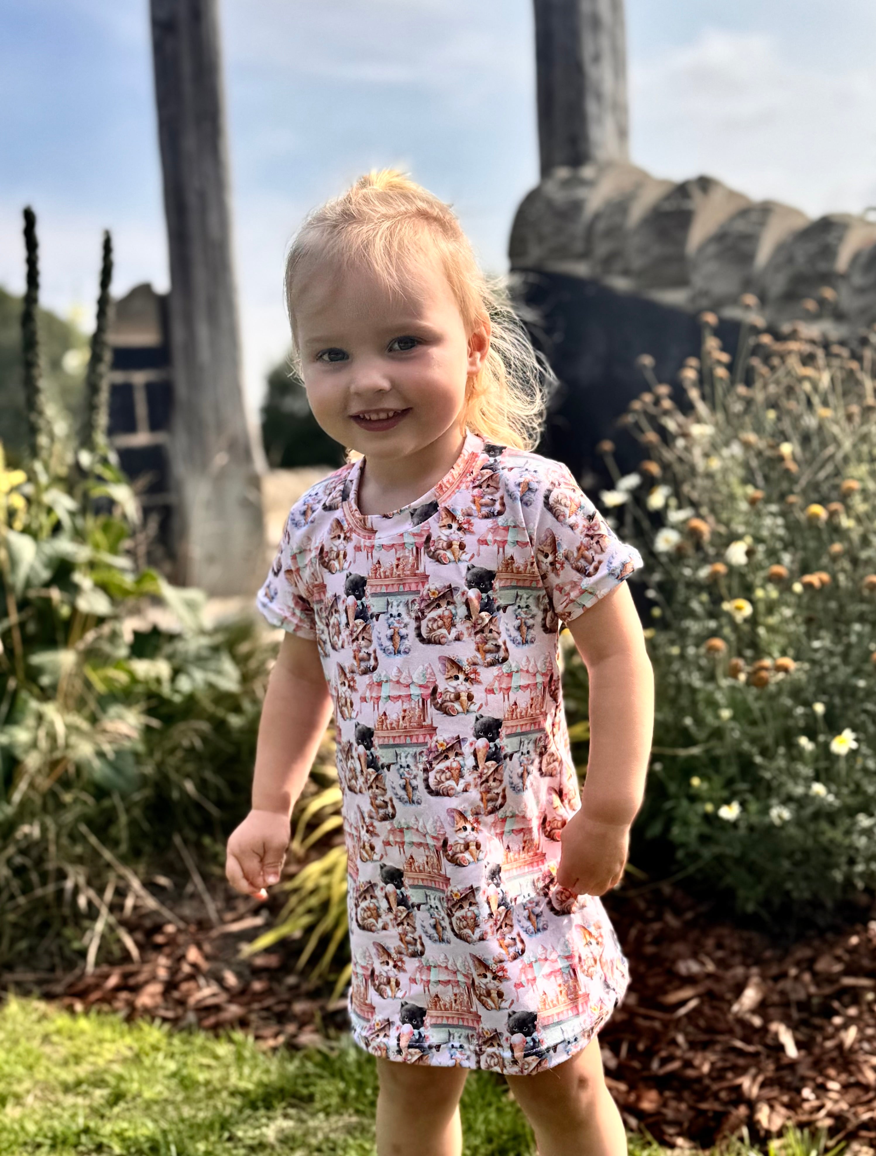 Young girl in a patterned dress standing outdoors with greenery in the background