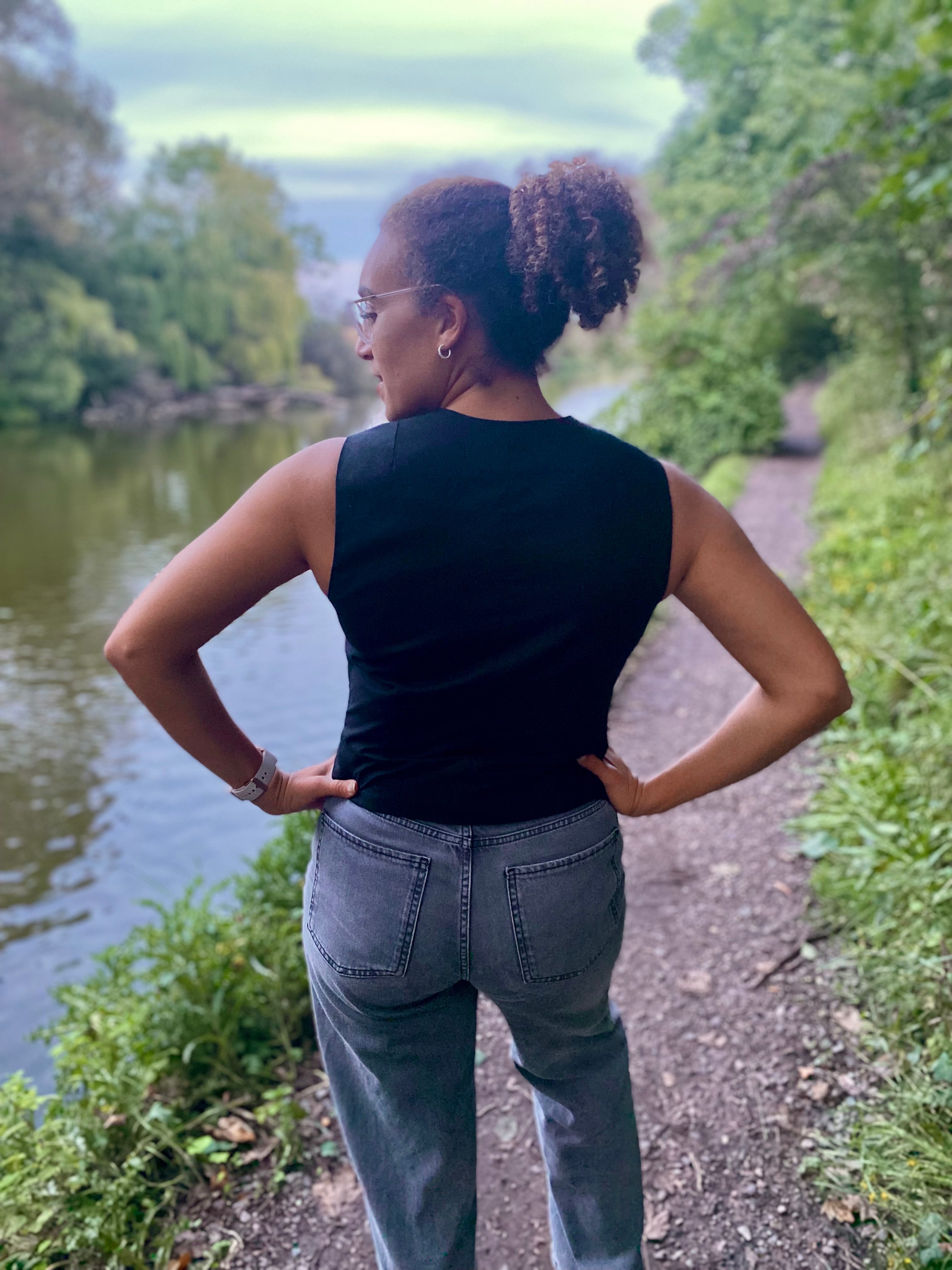 Person standing on a path by a river with trees in the background