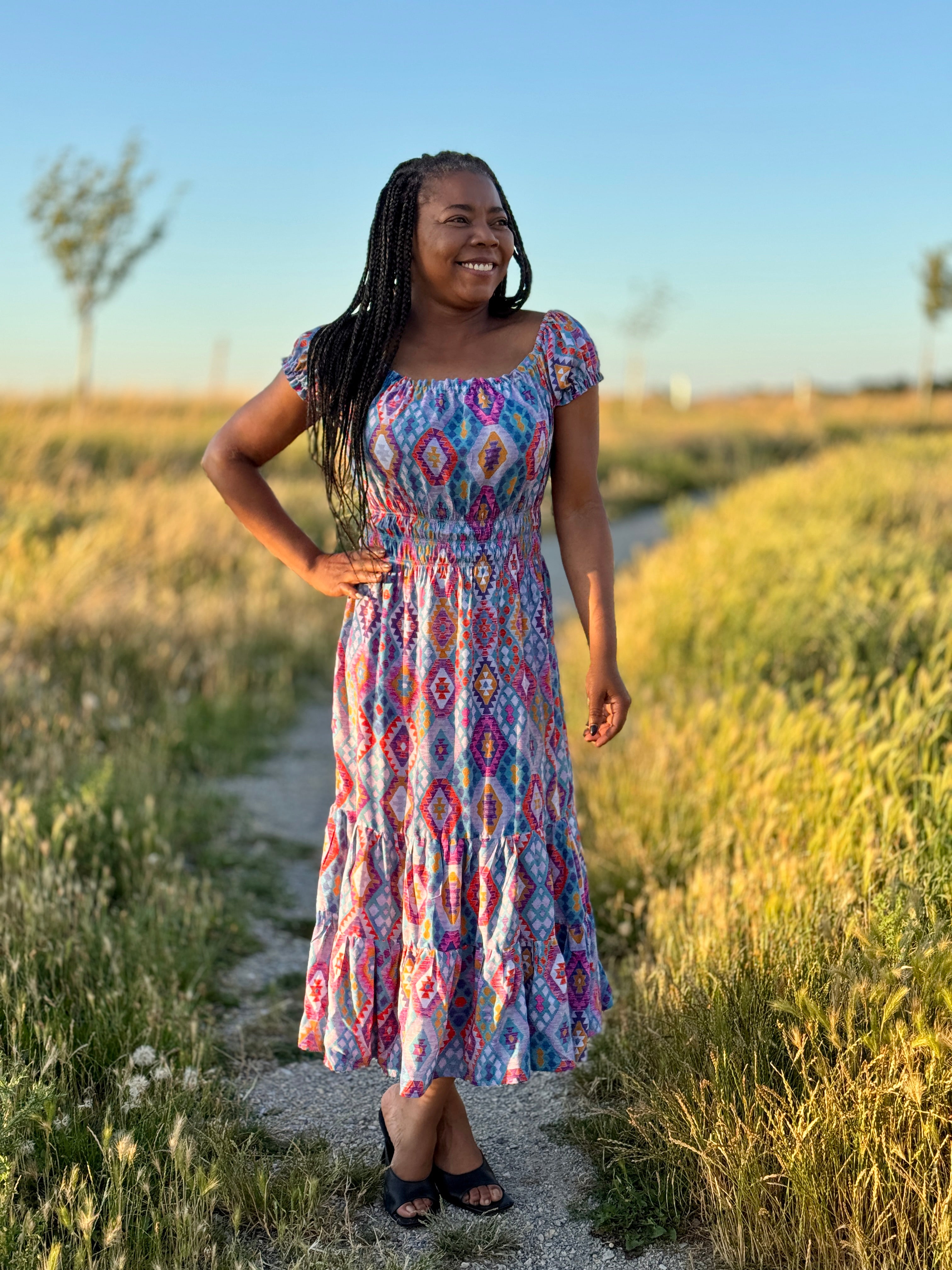 Woman in a colorful dress standing in a field with a clear sky.
