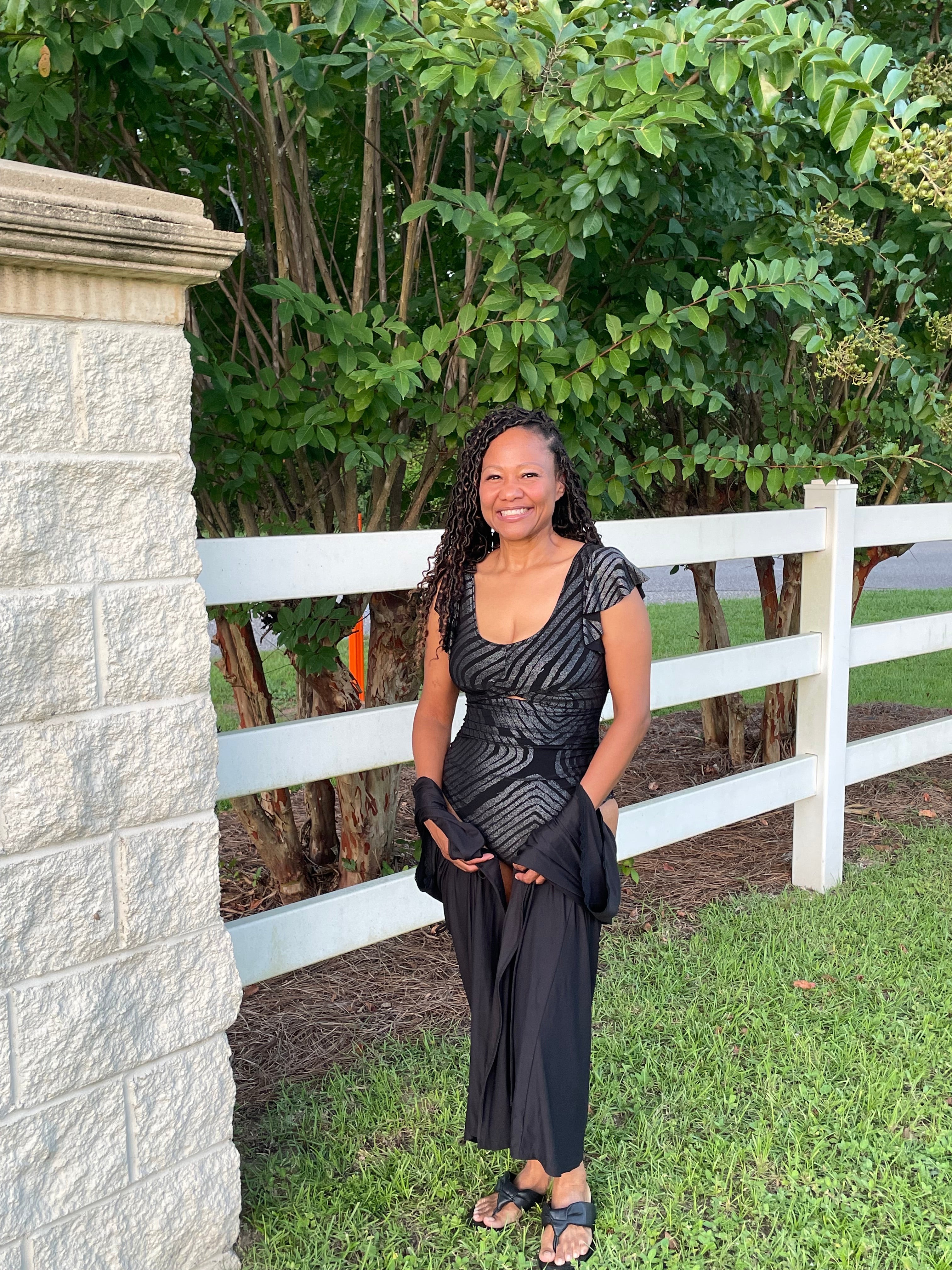 Woman in a black swimsuit standing on stone steps with greenery in the background
