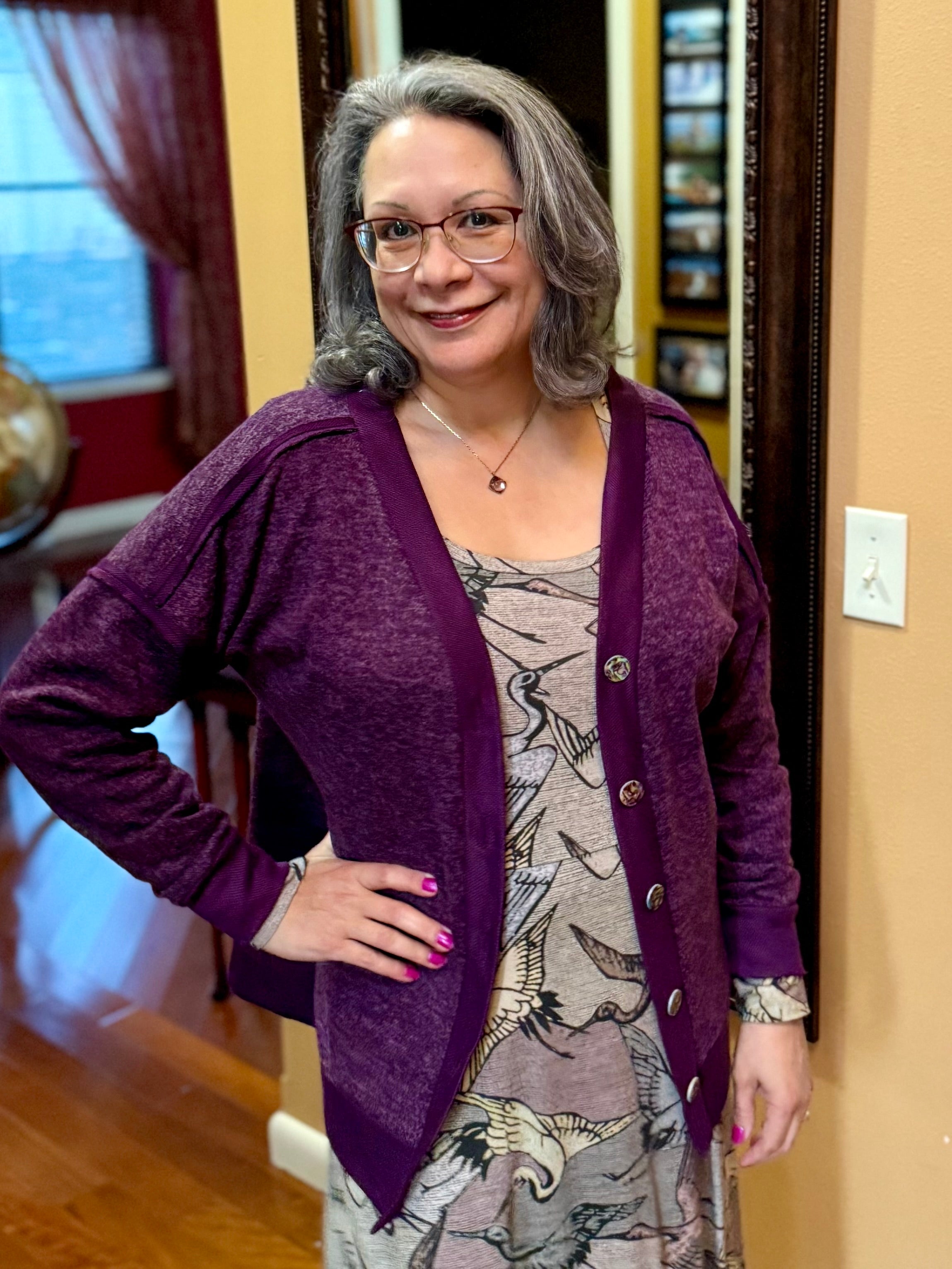Woman wearing a purple boxy cardigan over a patterned dress indoors.