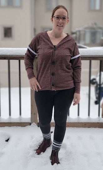 Person standing on a snow-covered deck wearing a brown cardigan and dark pants.