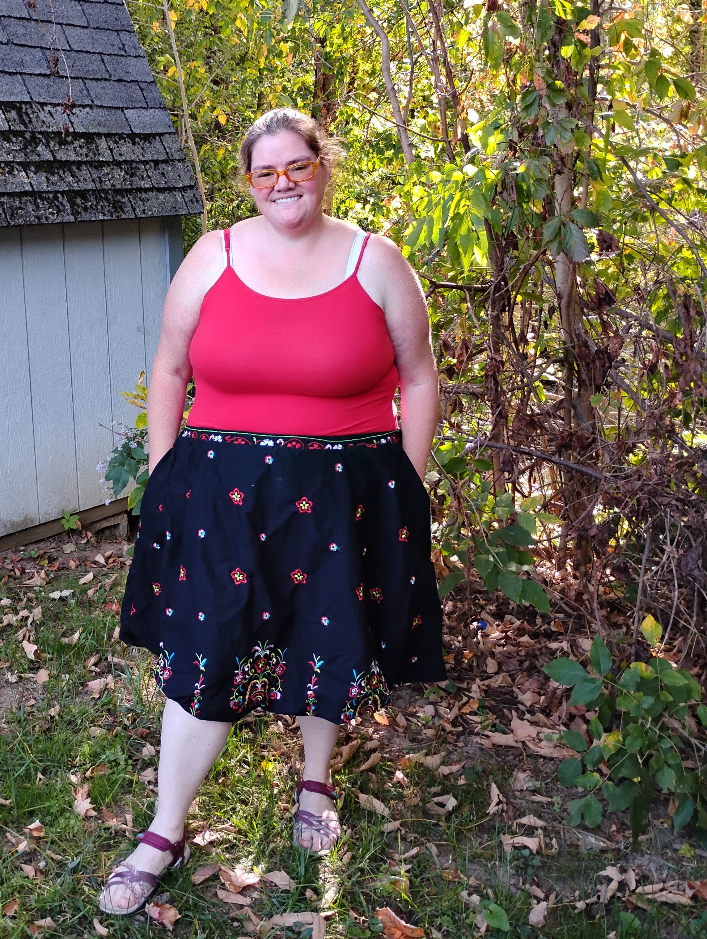 Person standing outdoors on a wooden deck with trees and grass in the background.