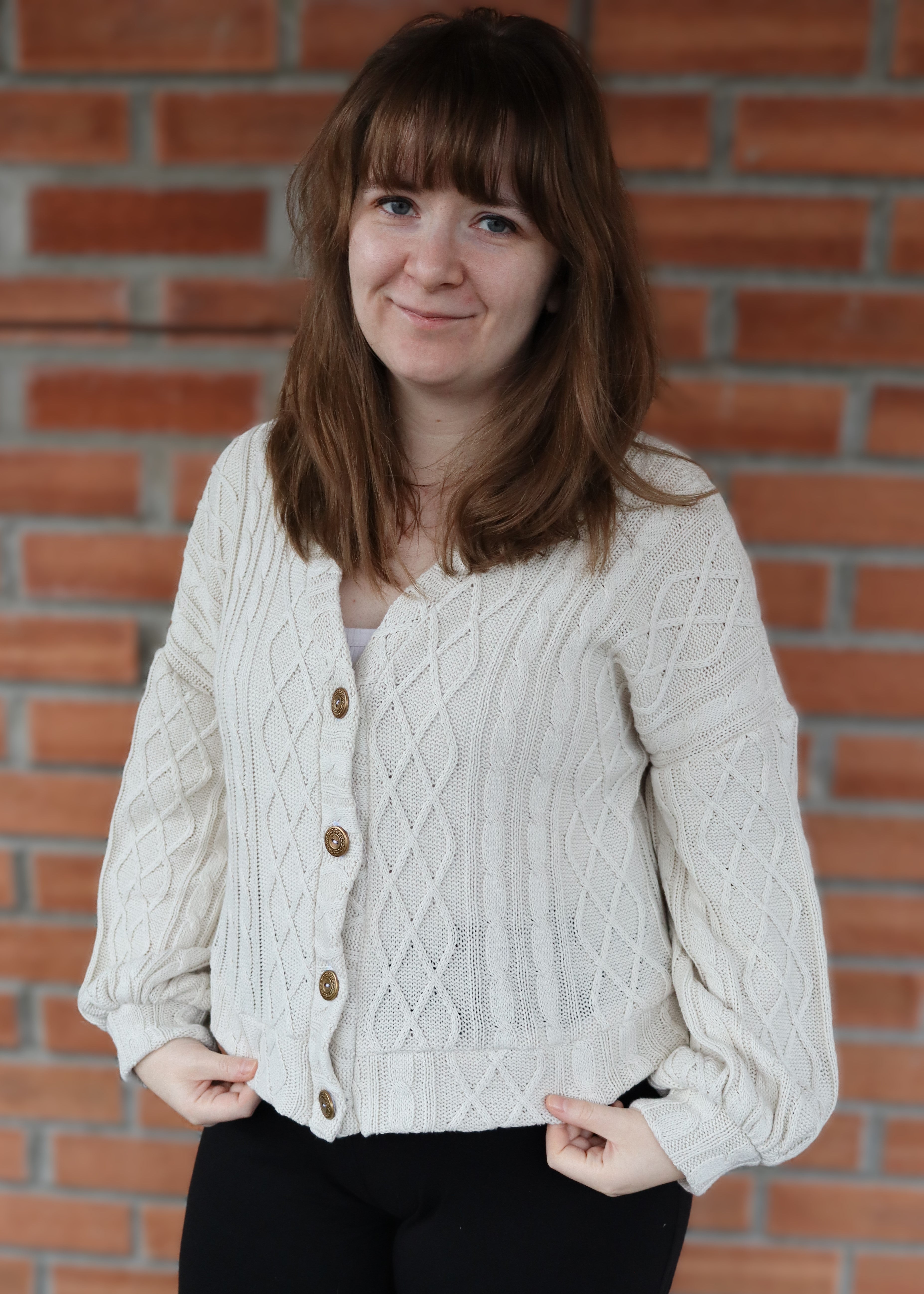 Woman wearing a cream cable knit cardigan against a brick wall
