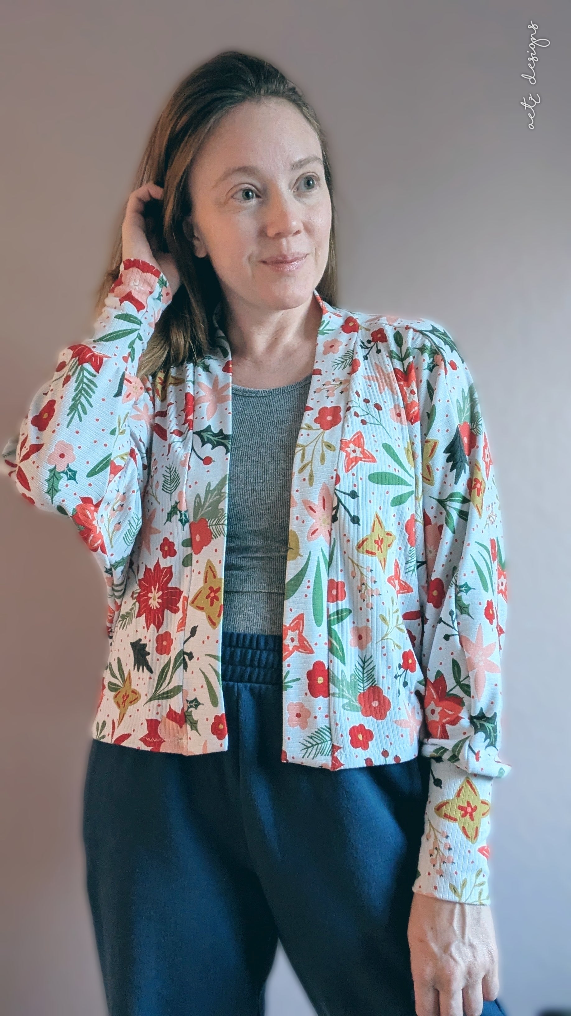 Woman wearing a floral crop cardigan with batwing design and tall cuffs with a plain background