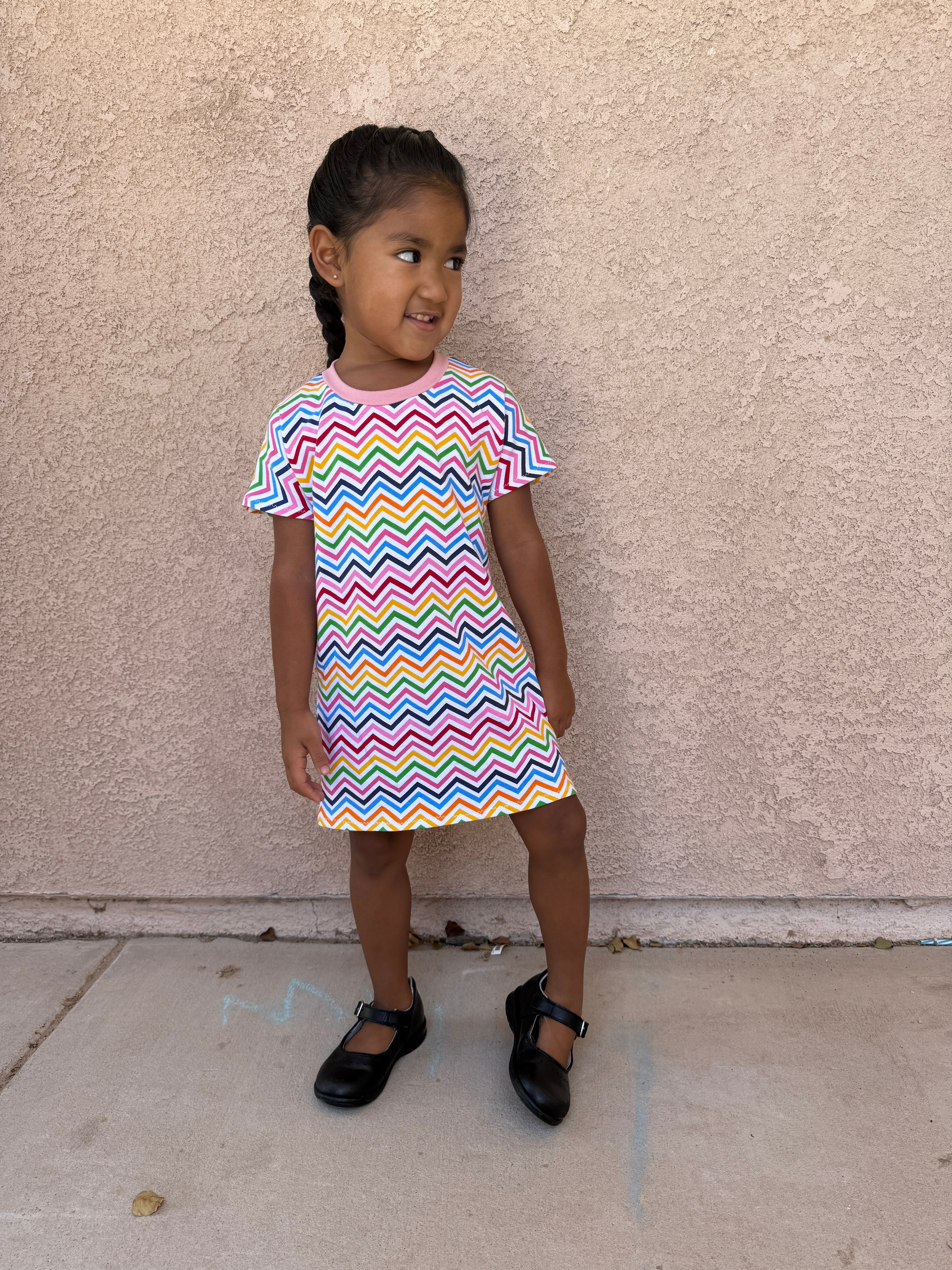Child wearing a colorful zigzag dress standing on a sidewalk. Dress made using Ellie and Mac's Kayla Crop Top and Dress sewing pattern. Fast sewing project.