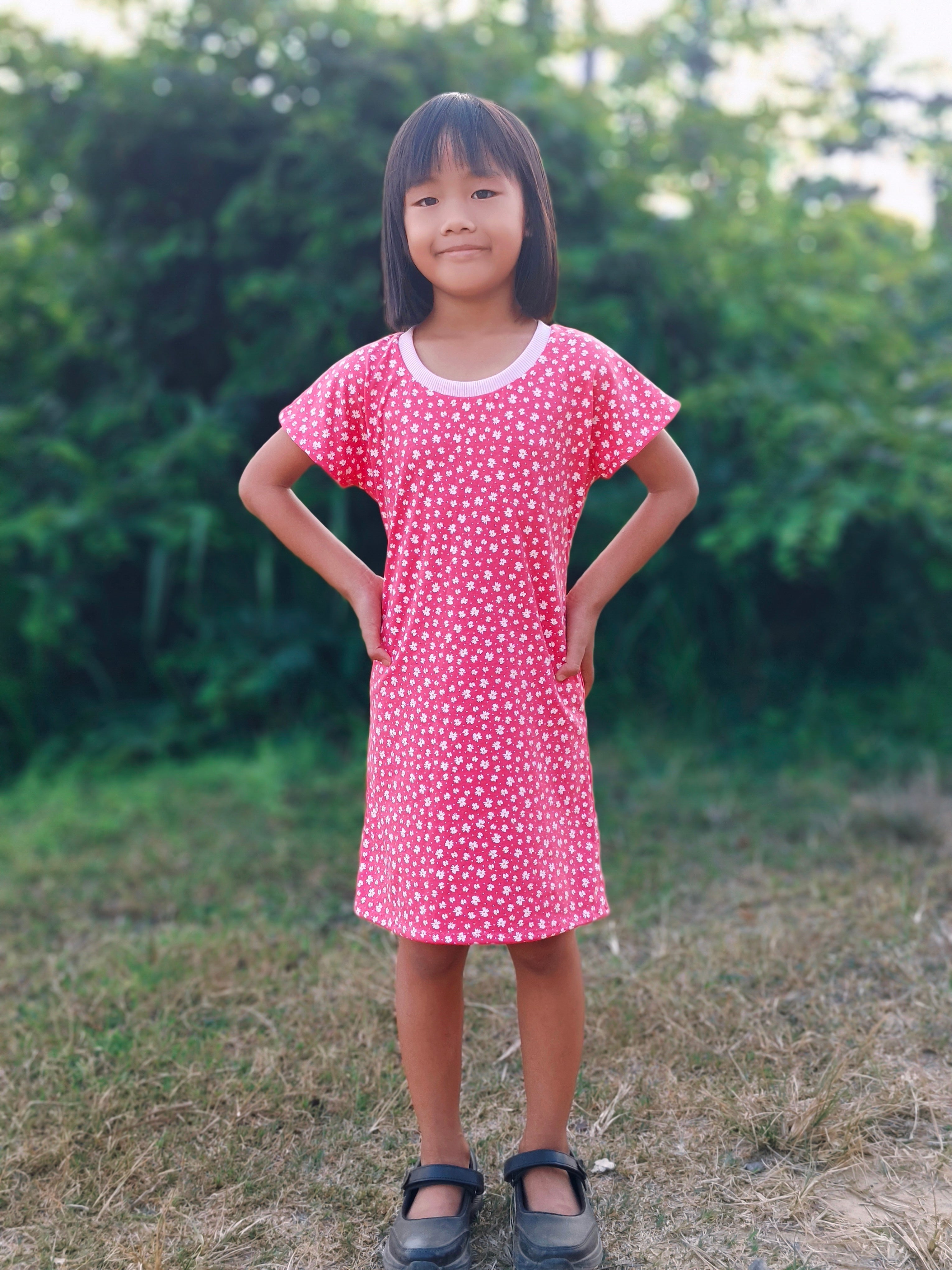 Girl wearing a pink dress with white polka dots standing outdoors.