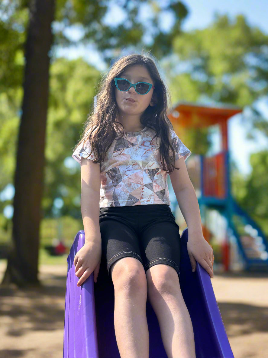 Young girl sitting on a purple slide at a playground with trees and equipment in the background.