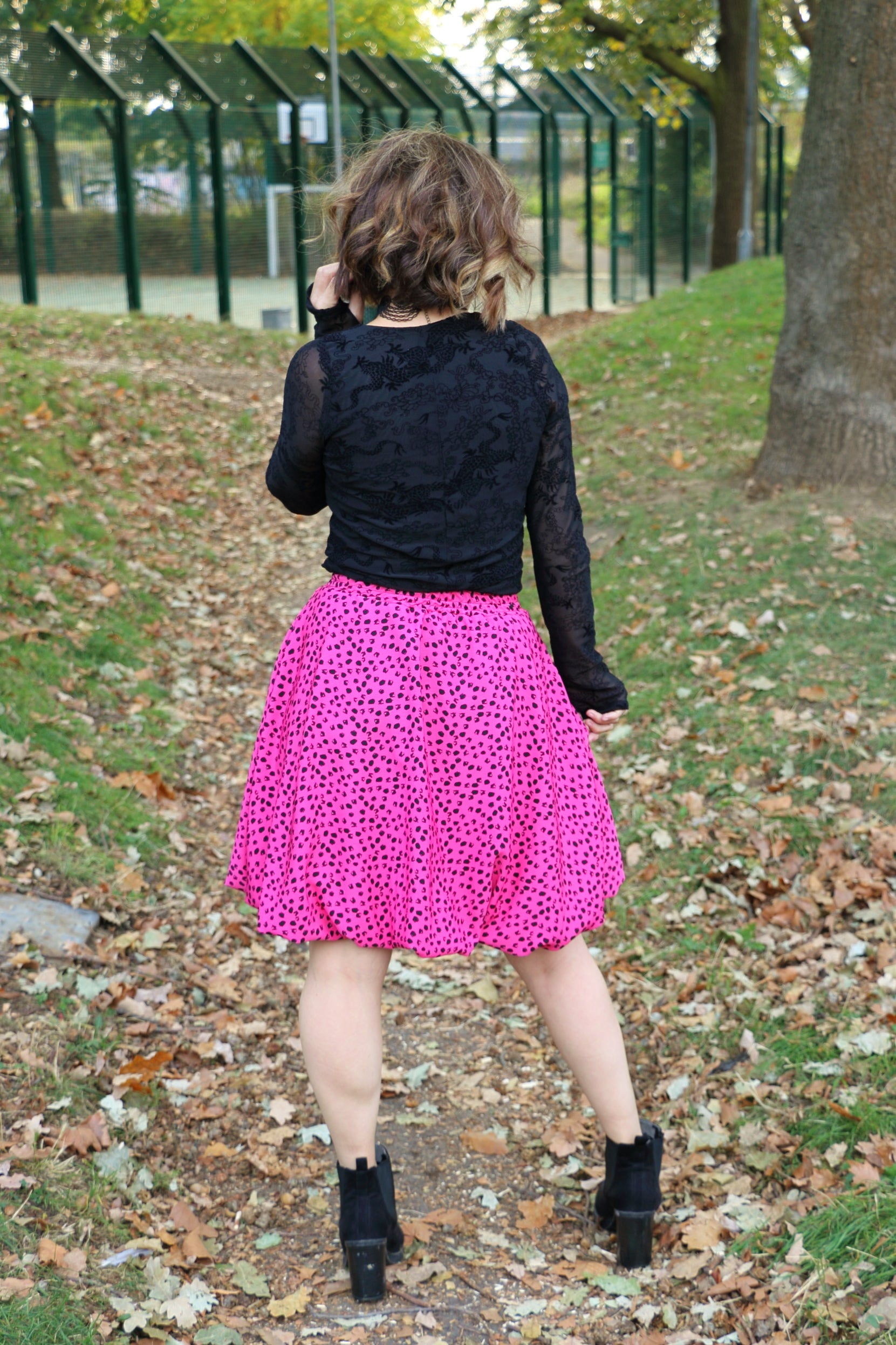 Person wearing a black top and pink bubble skirt walking on a leaf-covered path. Perfect date-night outfit made using Ellie and Mac PDF patterns.