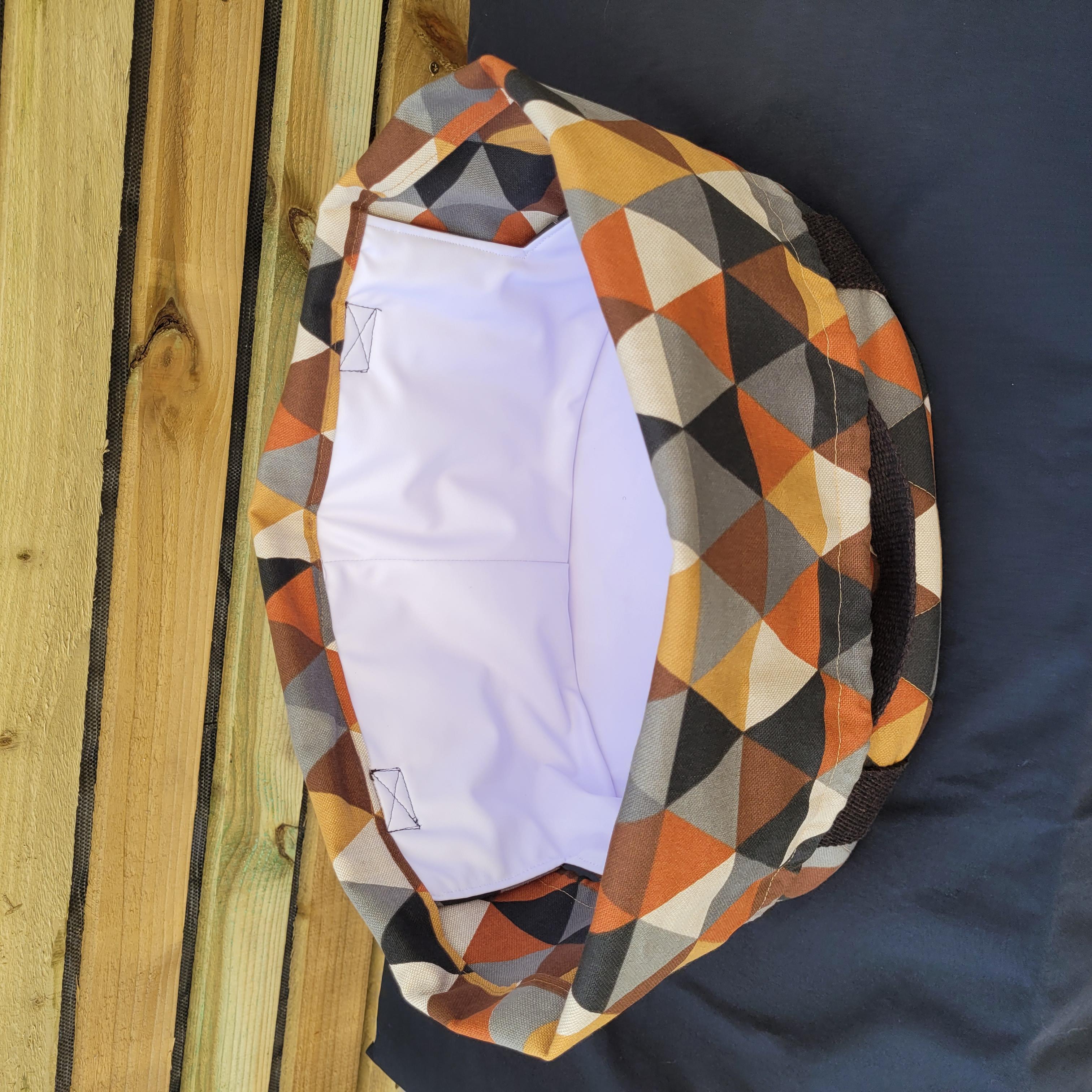 Colorful geometric-patterned fabric slow cooker carrier, open and empty, on a wooden surface. This carrier was made using the warm and cozy slow cooker carrier pattern by Ellie and Mac sewing patterns.