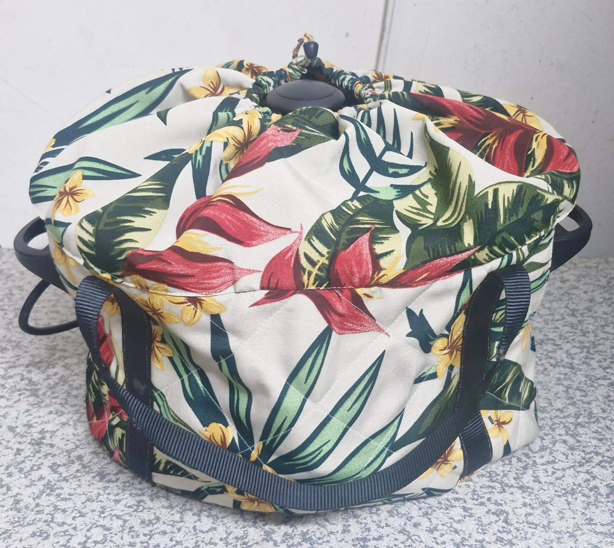 Tropical floral patterned slow cooker bag with a strap on a textured surface. Insulated and quilted to keep your food warm.
