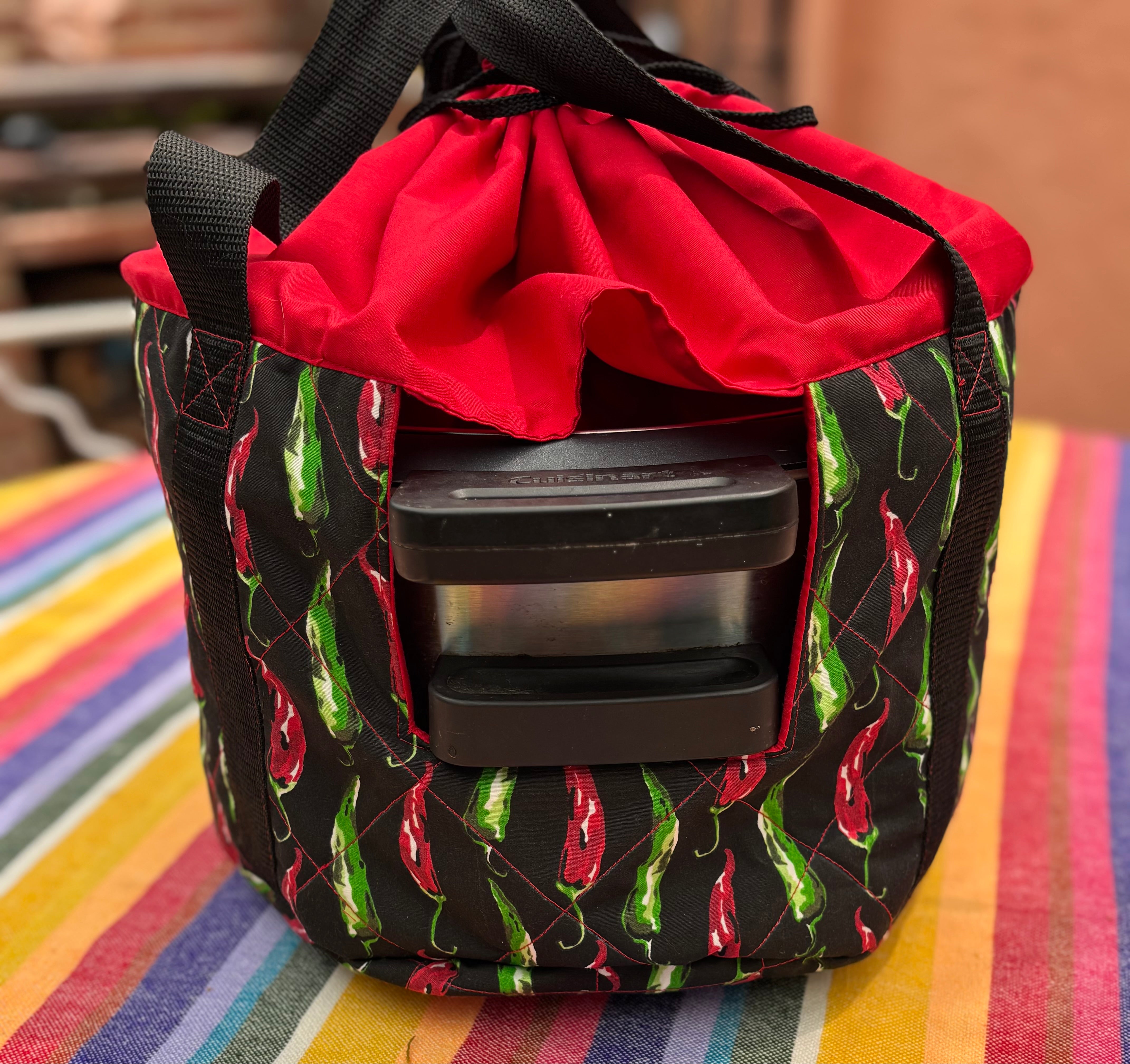 Insulated slow cooker bag with red top and black and green chili pepper pattern on a colorful striped surface. Sewn using the Ellie and Mac Warm and Cozy pattern.