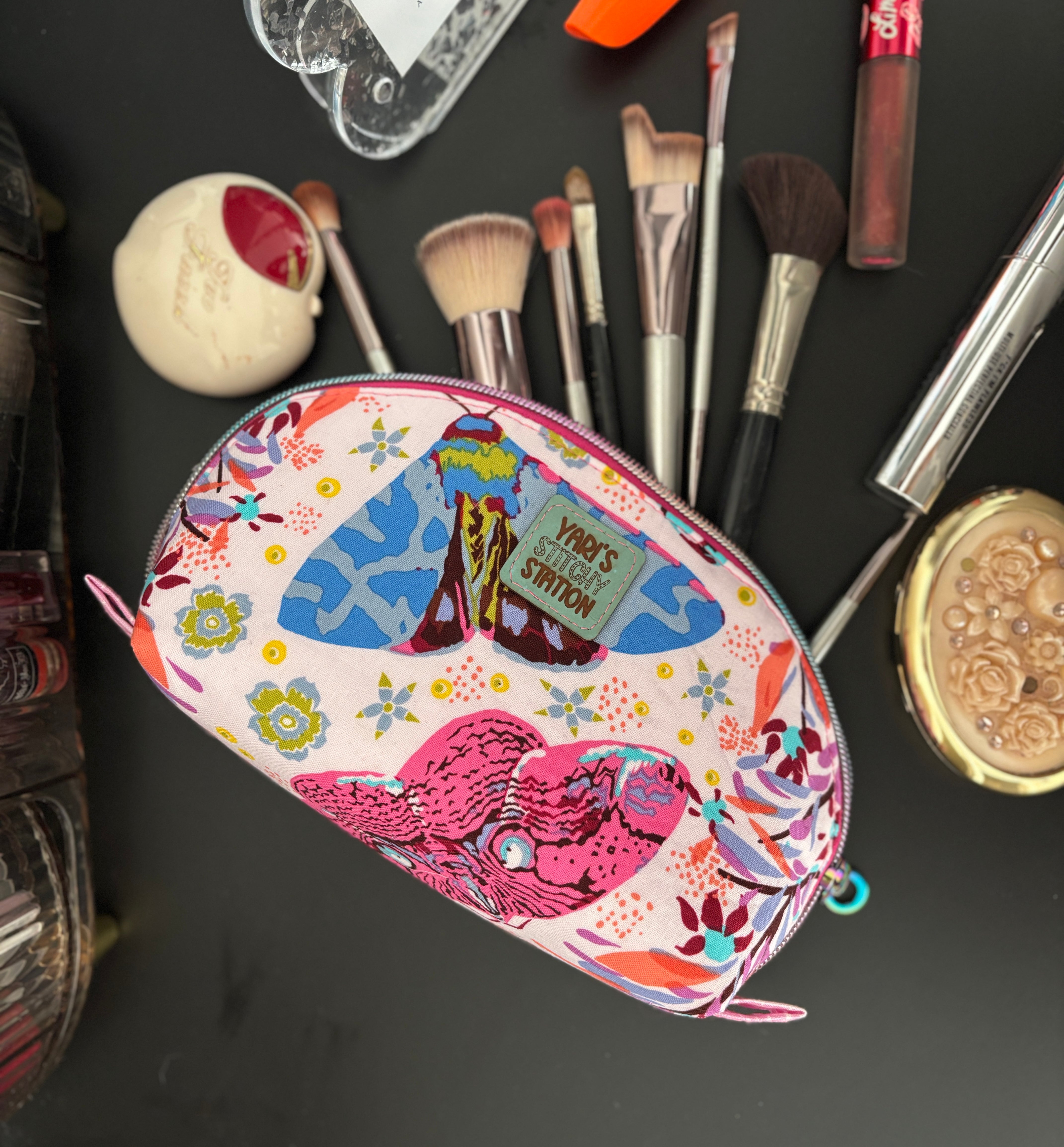 Tessa Makeup pouch with colorful design surrounded by makeup brushes and items on a dark surface. DIY zippered pouch.