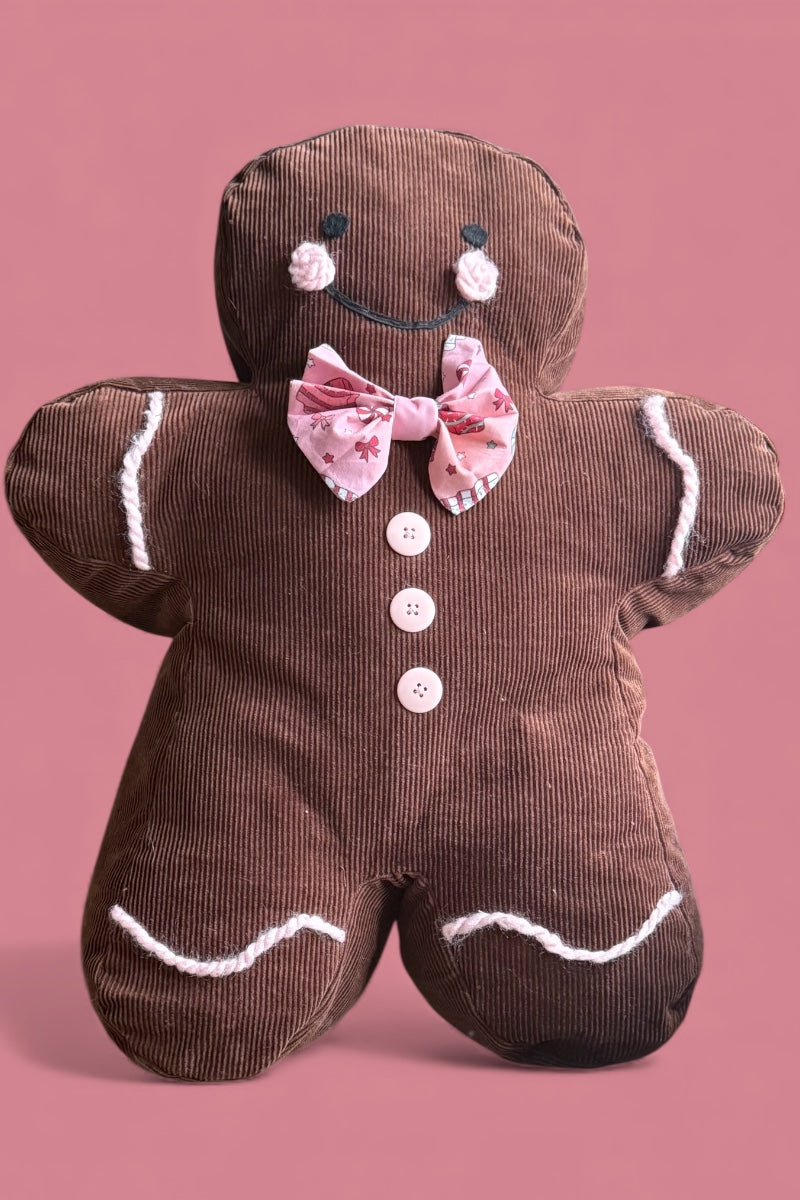 Plush gingerbread man toy with a pink bow tie on a pink background