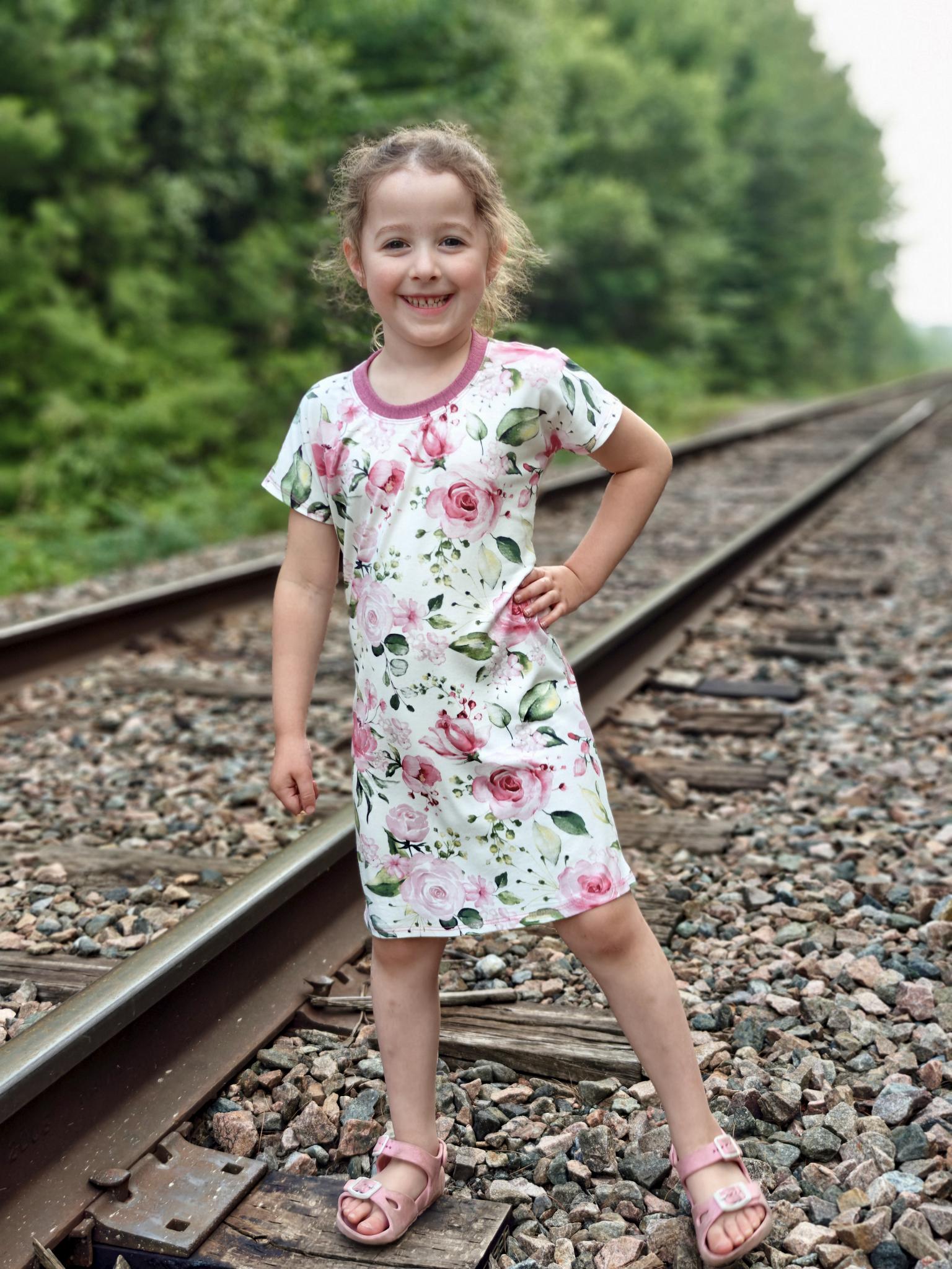 Young girl in a floral dress standing on train tracks with greenery in the background