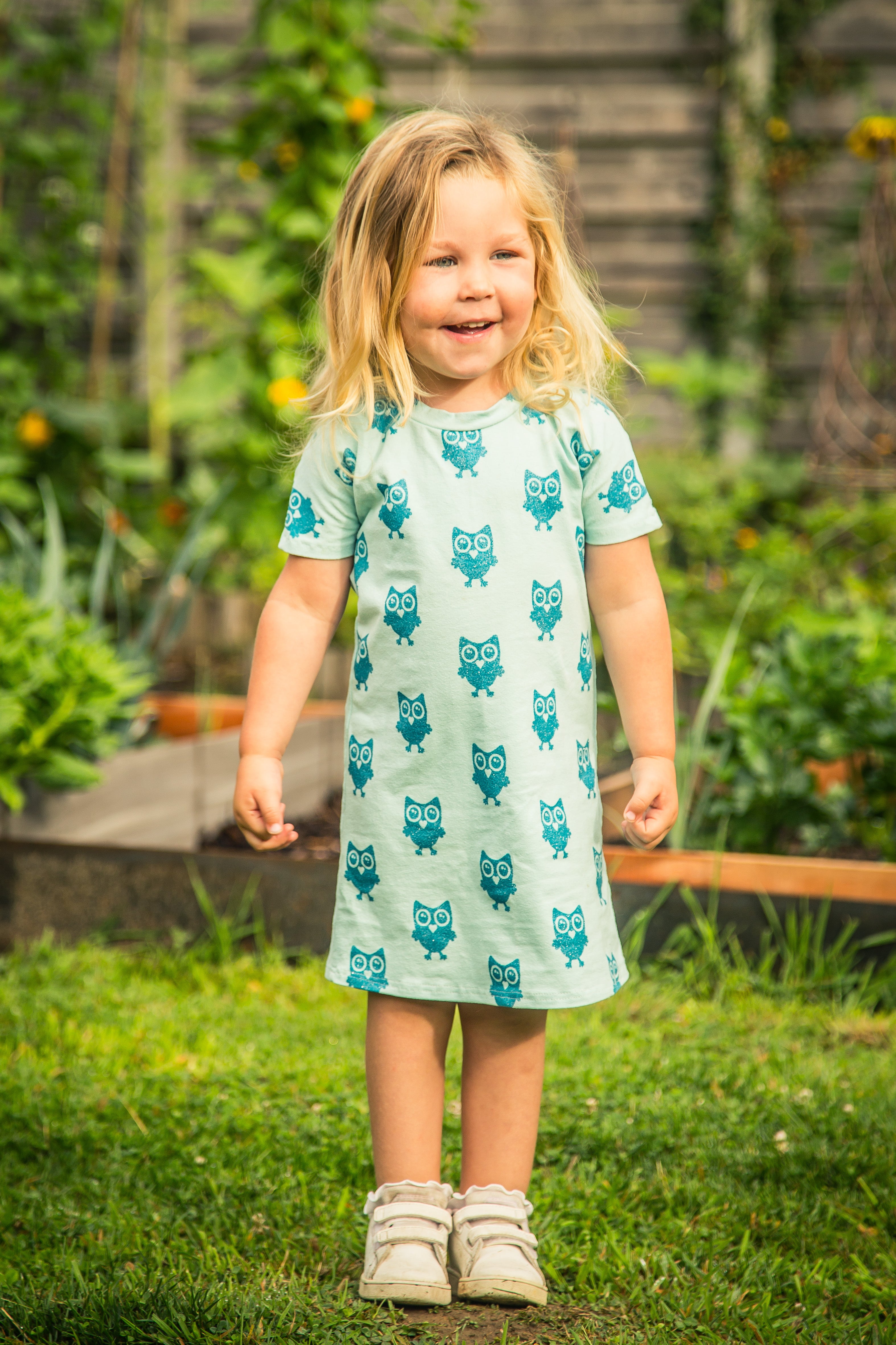 Young girl wearing a light blue dress with owl patterns in a garden setting.