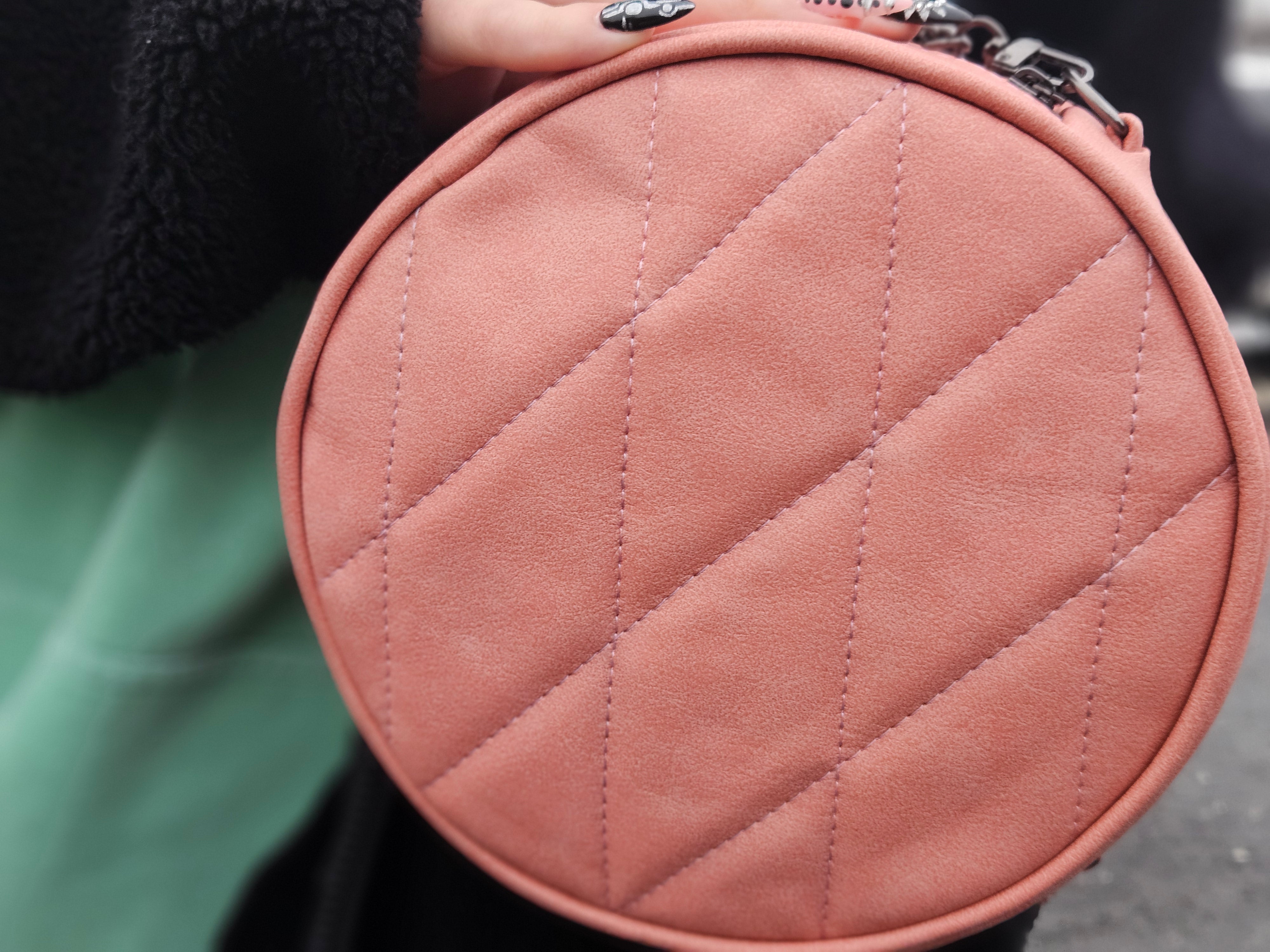 Close-up of a pink quilted handbag held by a person.