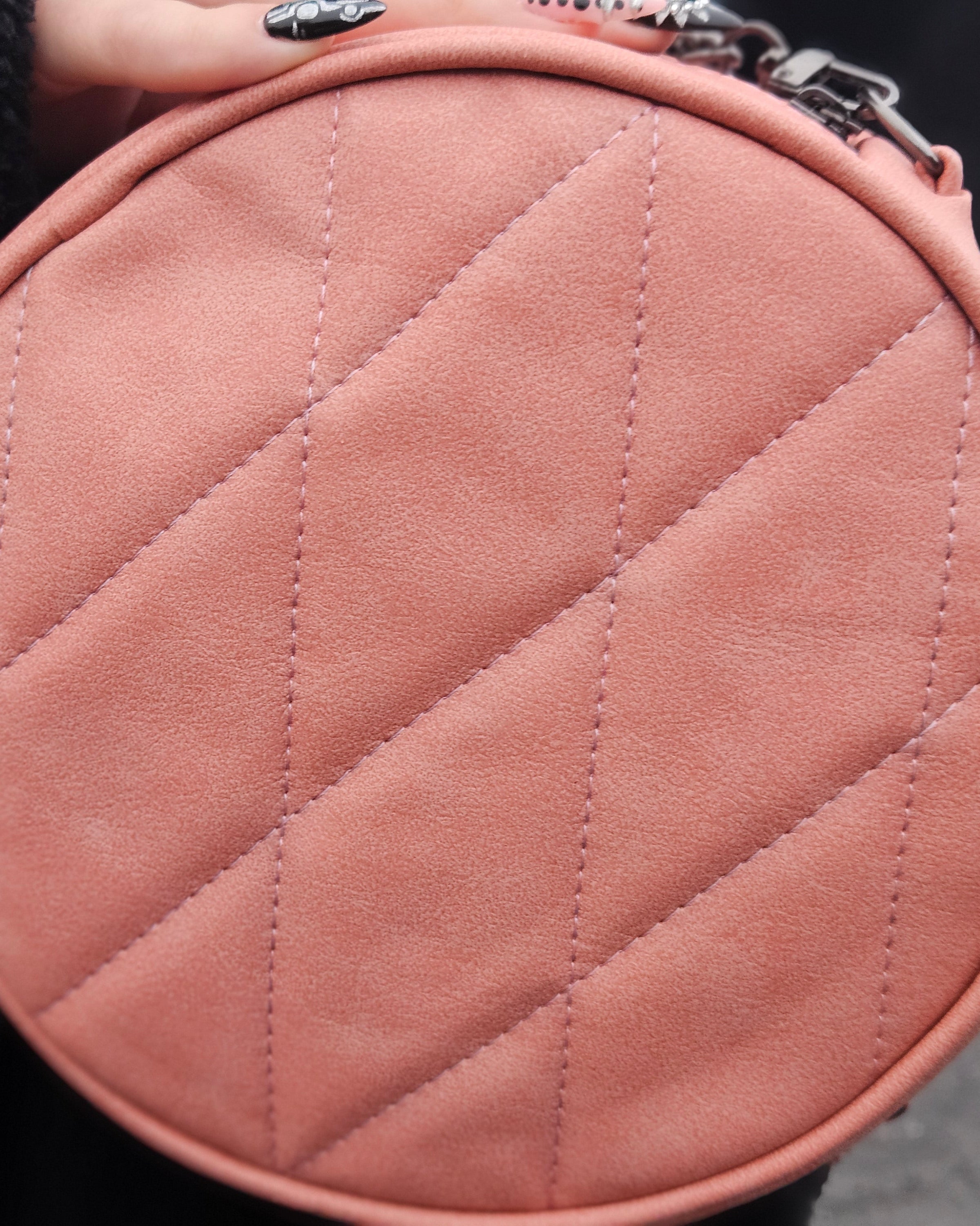 Close-up of a pink quilted handbag held by a person.
