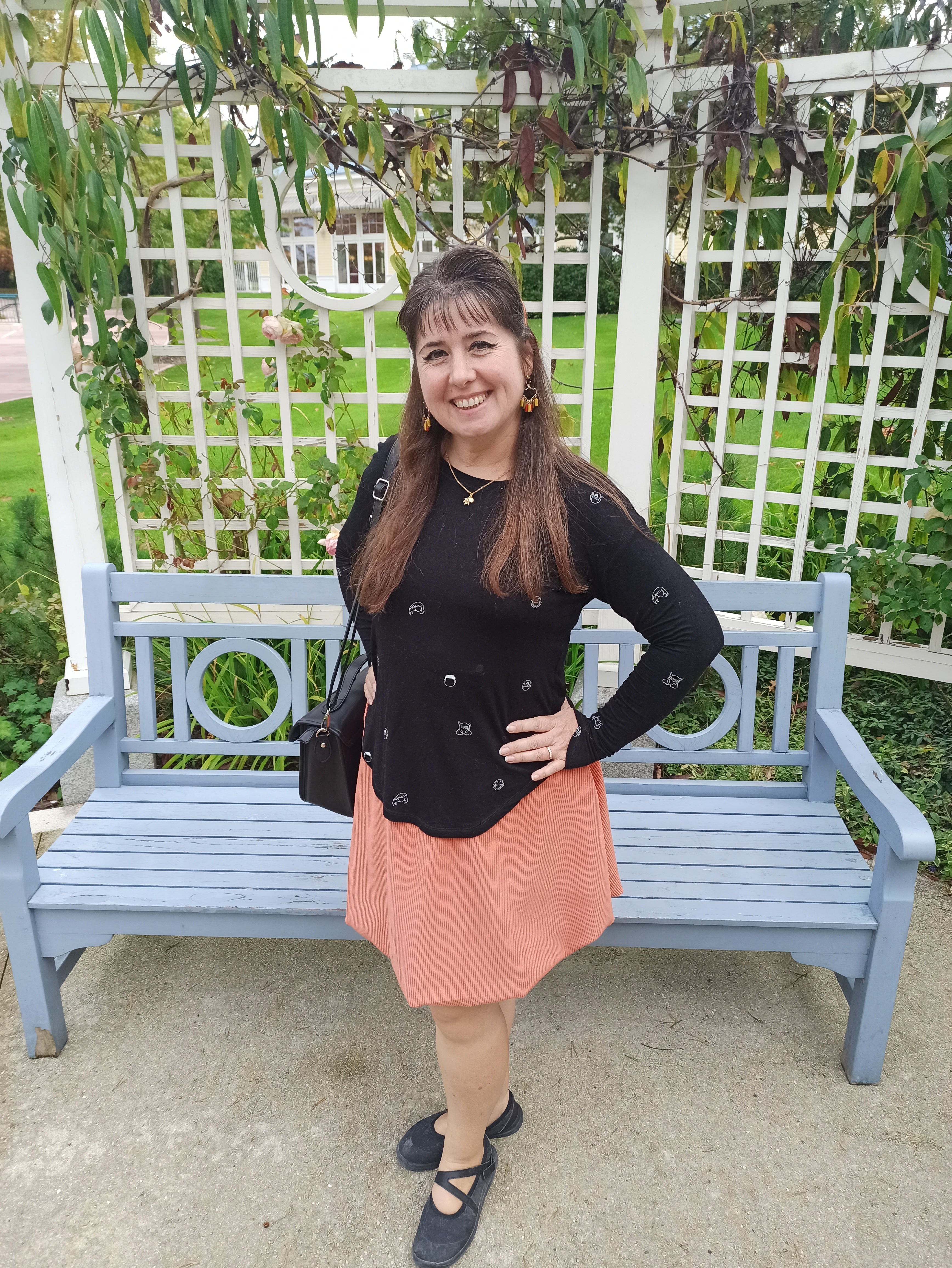 Woman standing next to a blue bench in a garden setting wearing an orange bubble skirt and black top for Halloween.