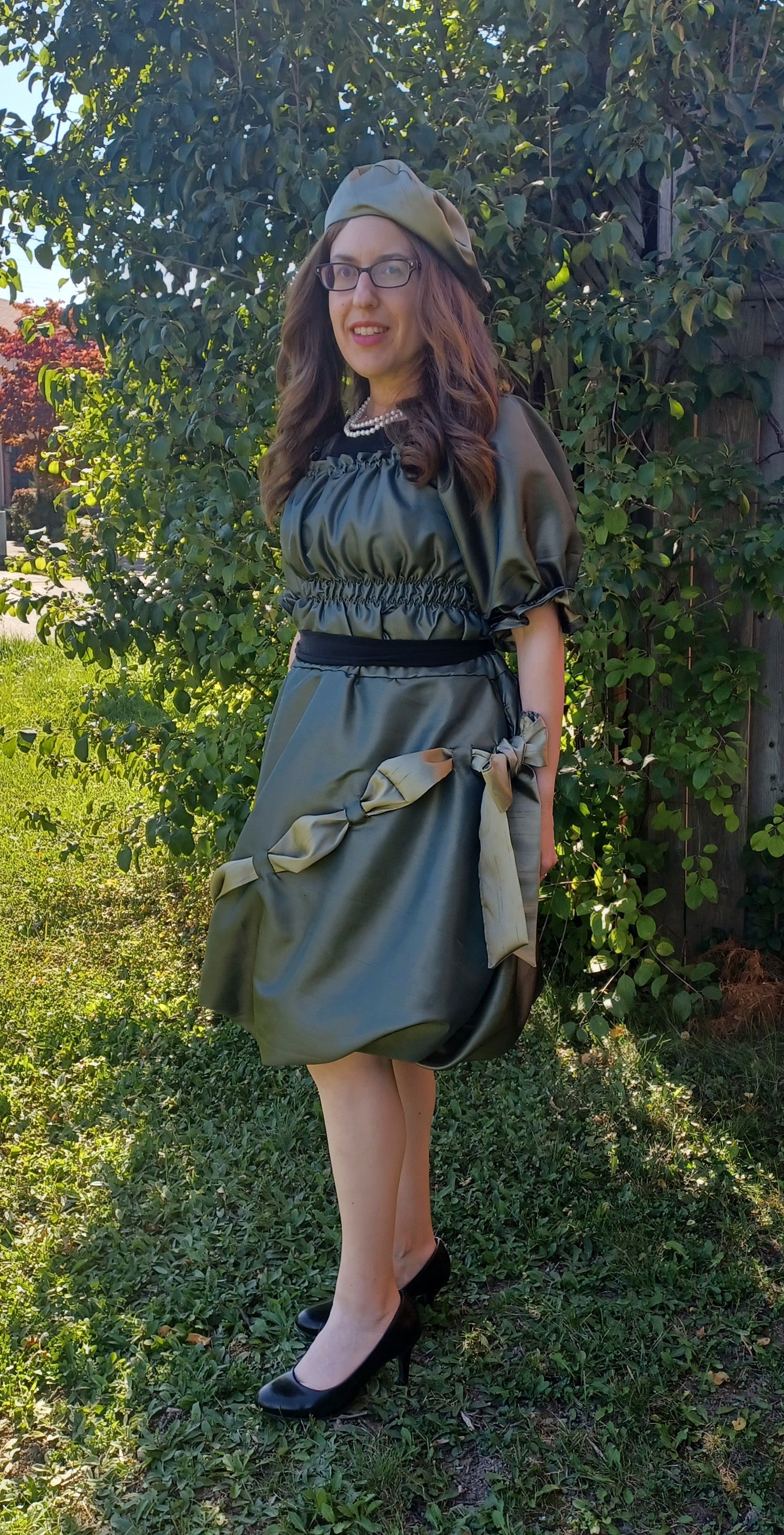 Woman in a green formal bubble skirt standing outdoors with trees in the background.