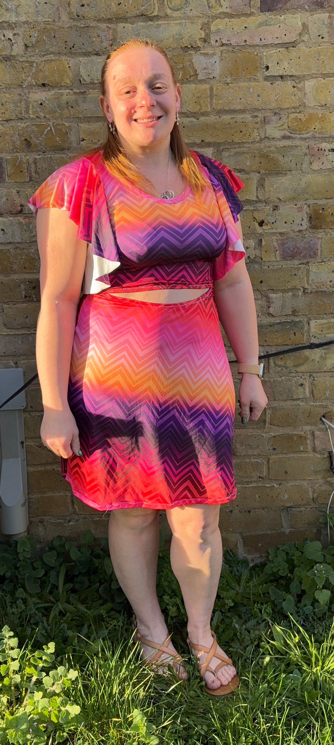Person wearing a colorful dress standing in front of a brick wall.