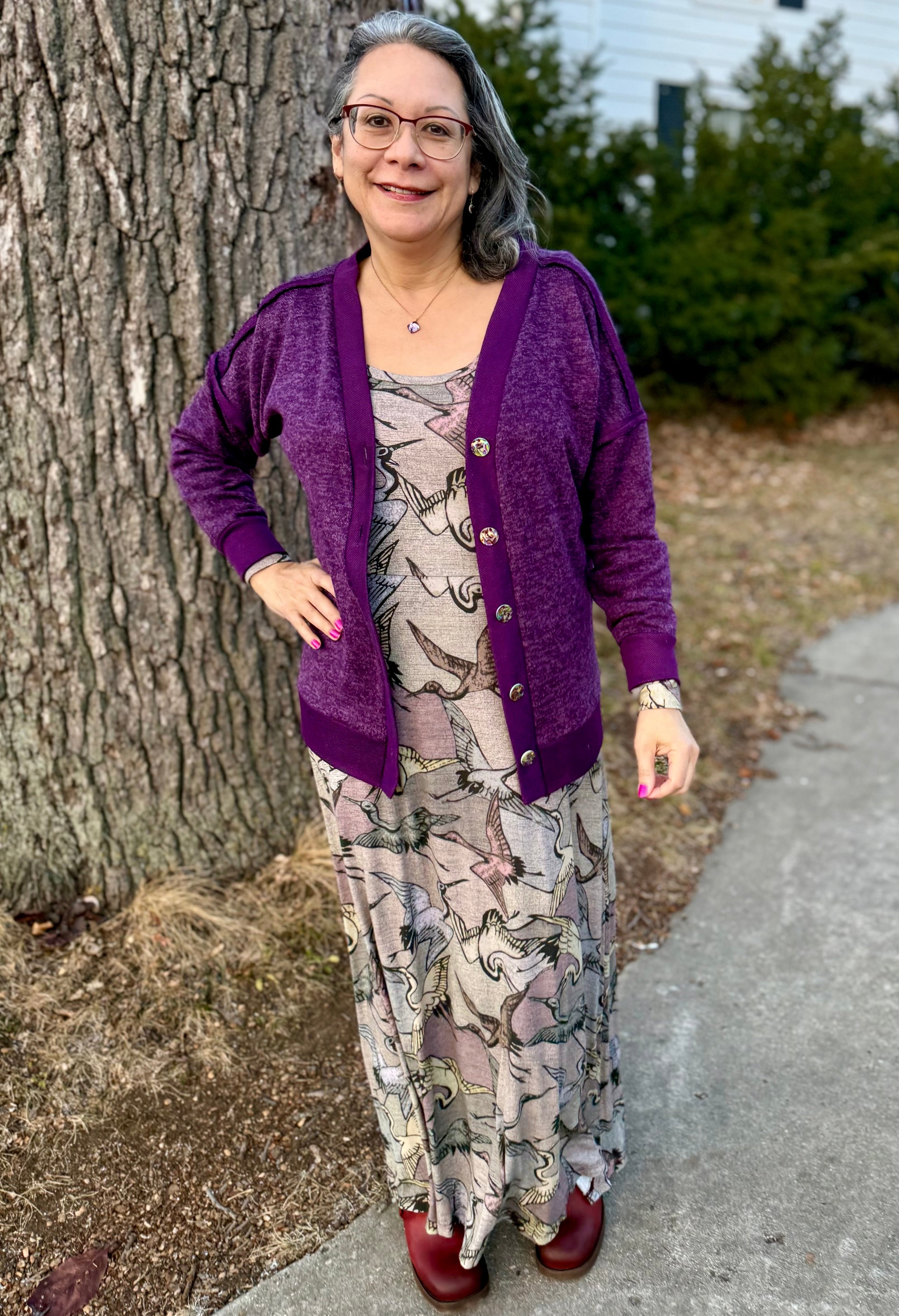 Woman wearing a purple brielle cardigan and patterned dress standing next to a tree.
