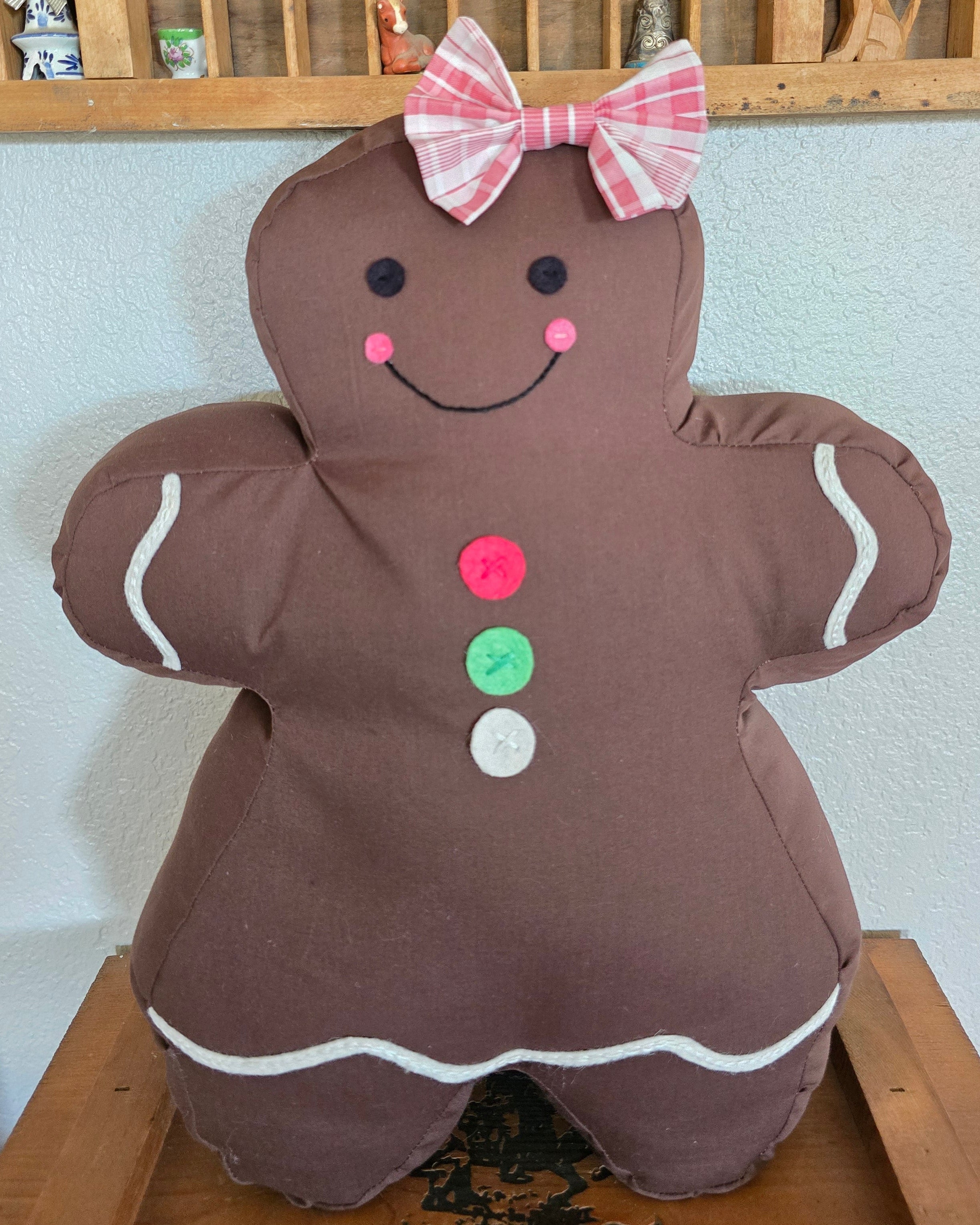 Gingerbread woman-shaped pillow on a shelf with a wooden bookshelf in the background