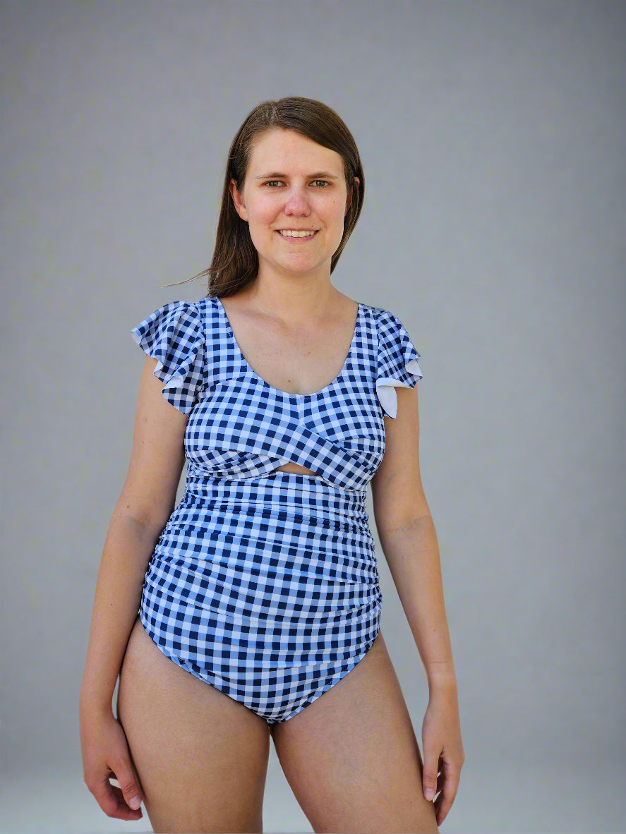 Woman wearing a blue and white checkered swimsuit standing against a white wall.
