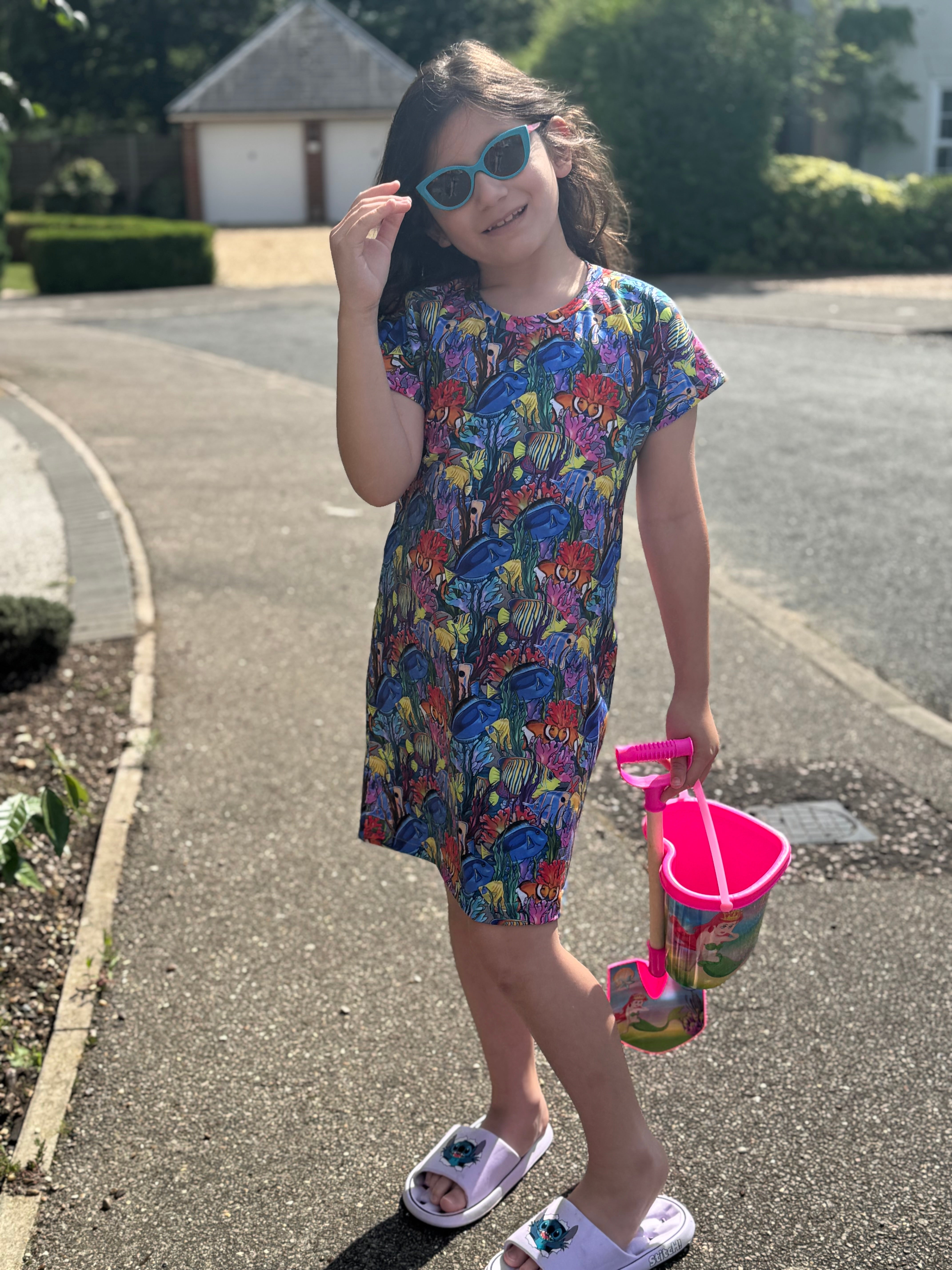 Young girl in a colorful dress with a toy pail on a driveway
