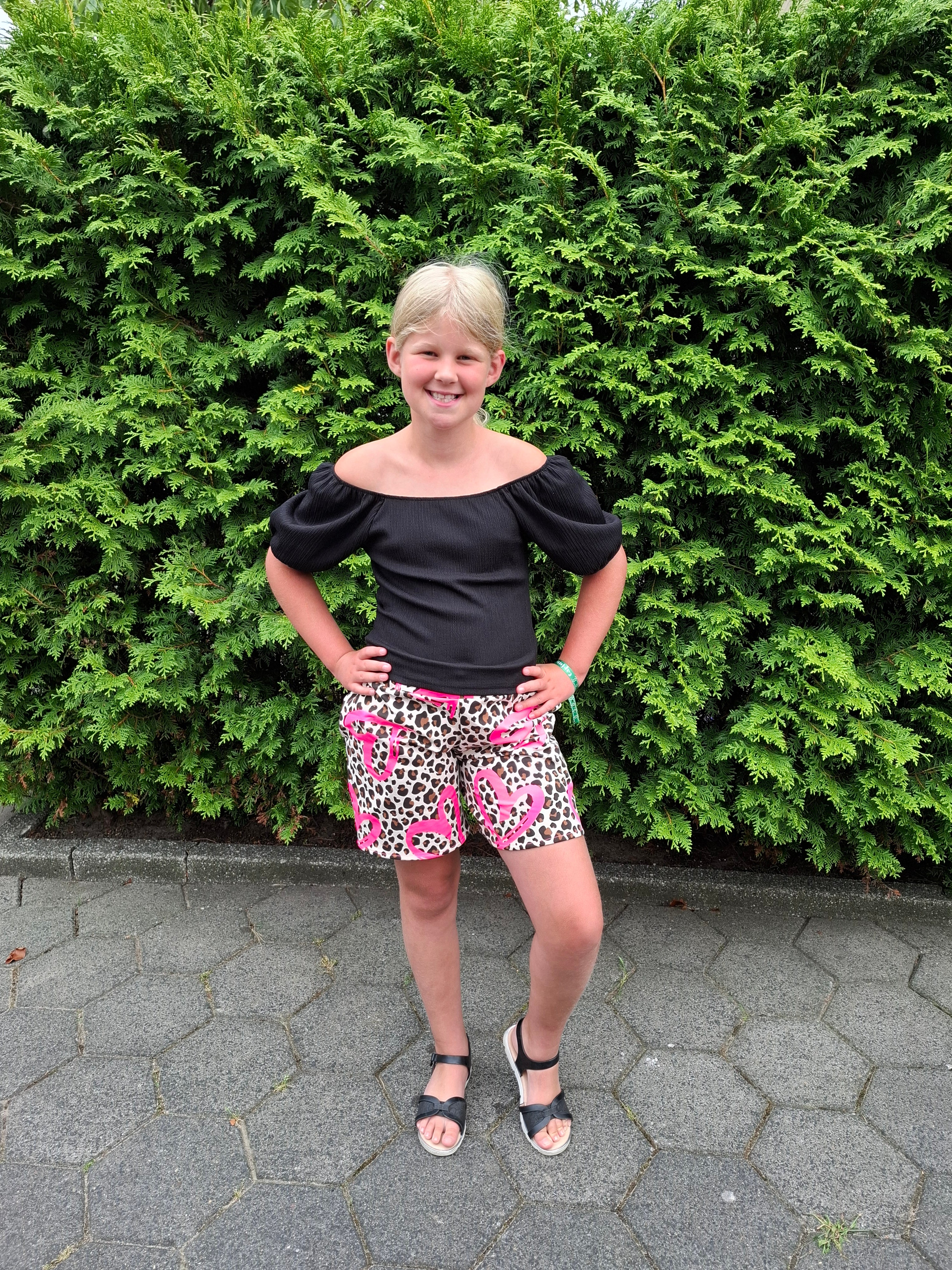 Girl standing next to a green bush on a paved path wearing a cute black top and knit shorts made using the Caleb Athletic Sewing Pattern by Ellie and Mac Patterns.