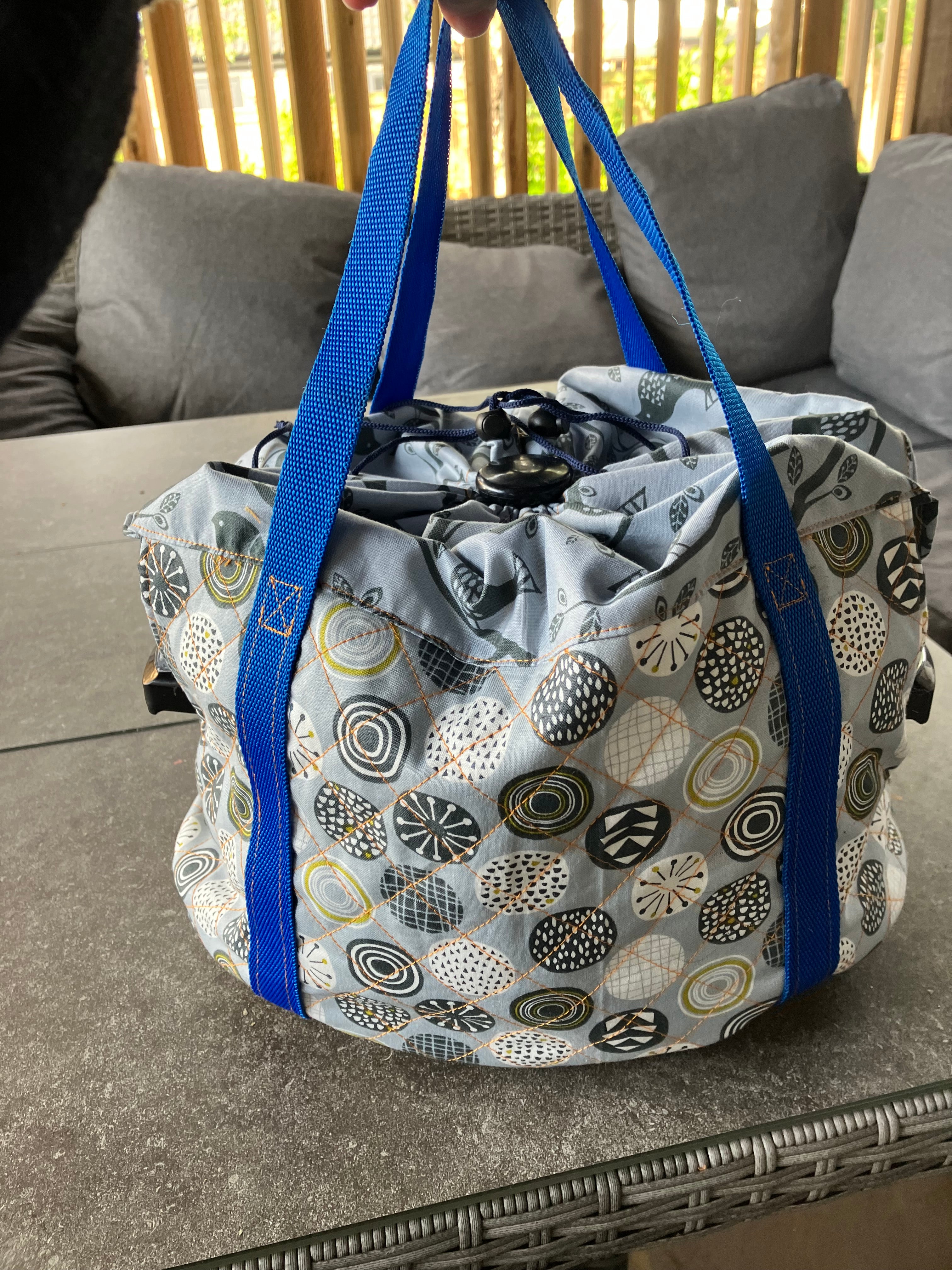 Patterned slow cooker carrier bag with blue straps on a textured surface.