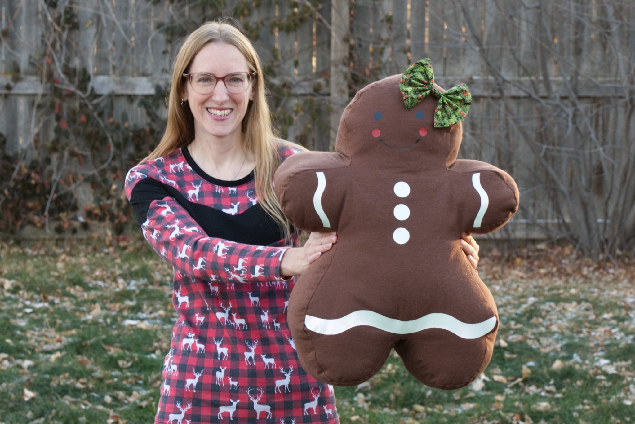 Woman holding a large plush gingerbread woman outdoors.