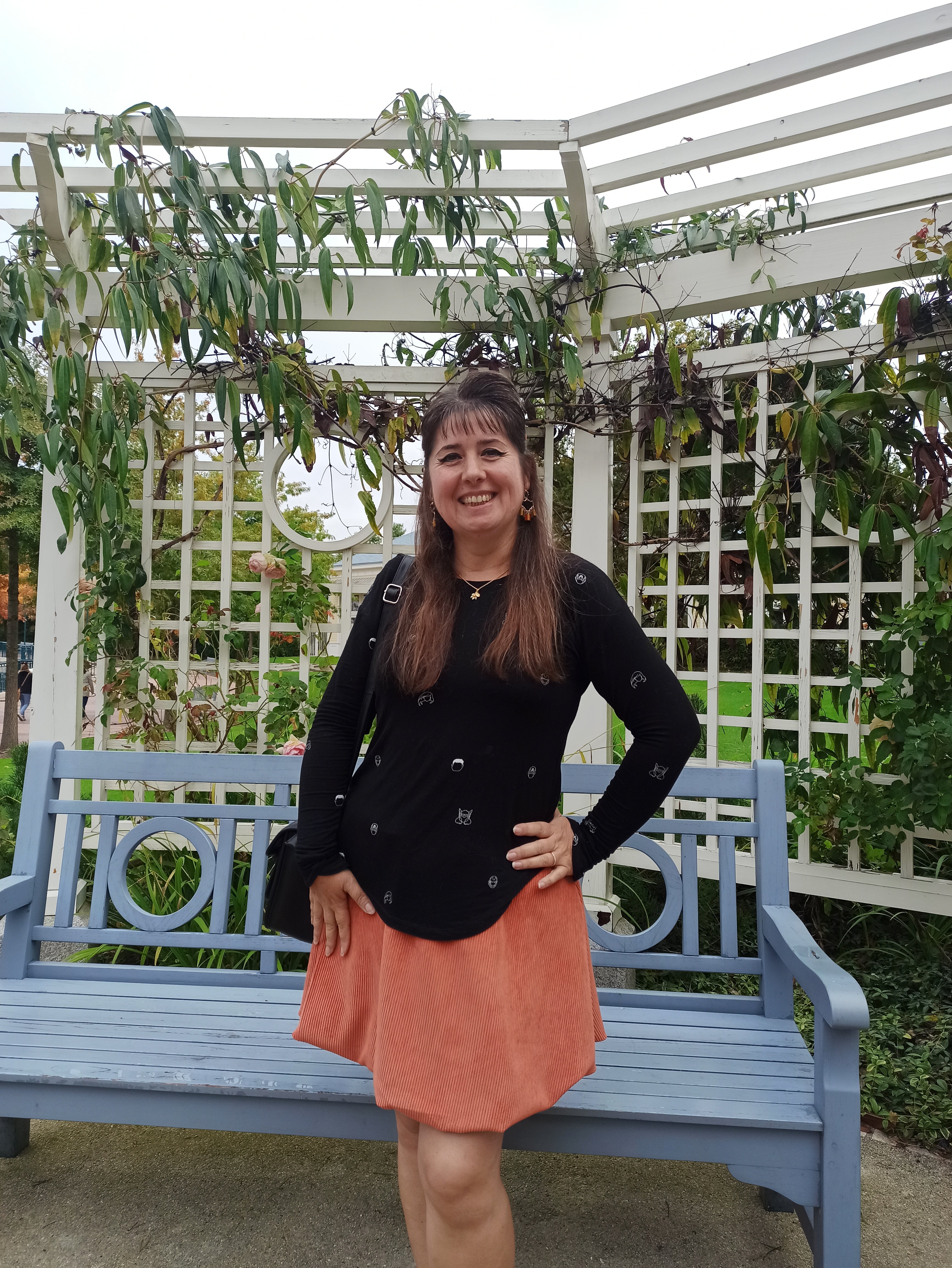 Woman standing outdoors with a blue bench and greenery in the background. Wearing an orange bubble skirt she made using the Sadie Bubble Skirt Pattern.