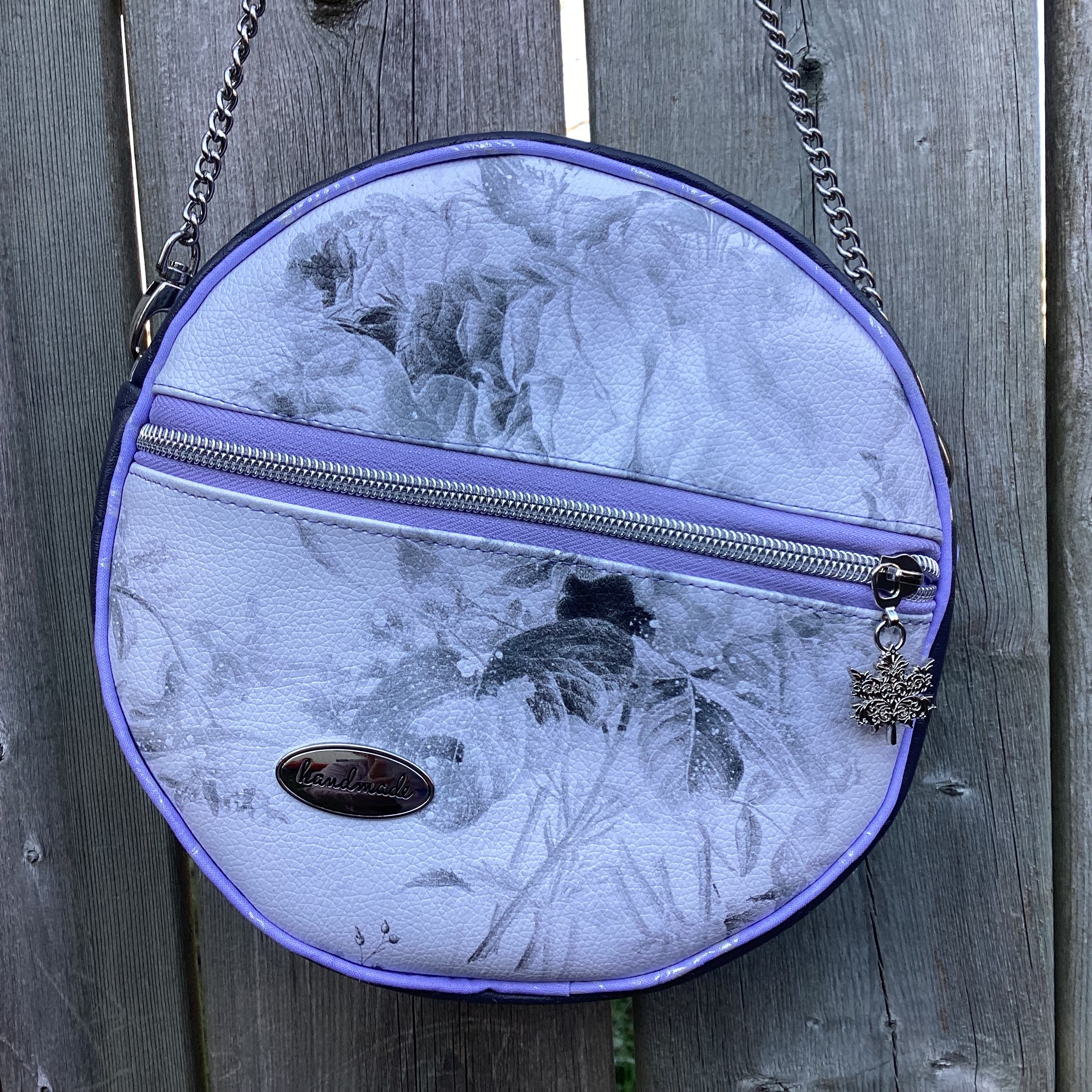 Round handbag with floral pattern and chain strap on wooden surface