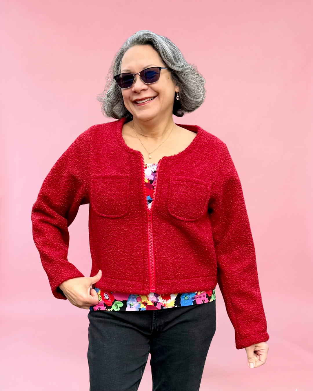 Woman wearing a red bloucle fabric jacket and colorful pants against a pink background. Jacket sewing pattern by Ellie and Mac PDF sewing patterns.