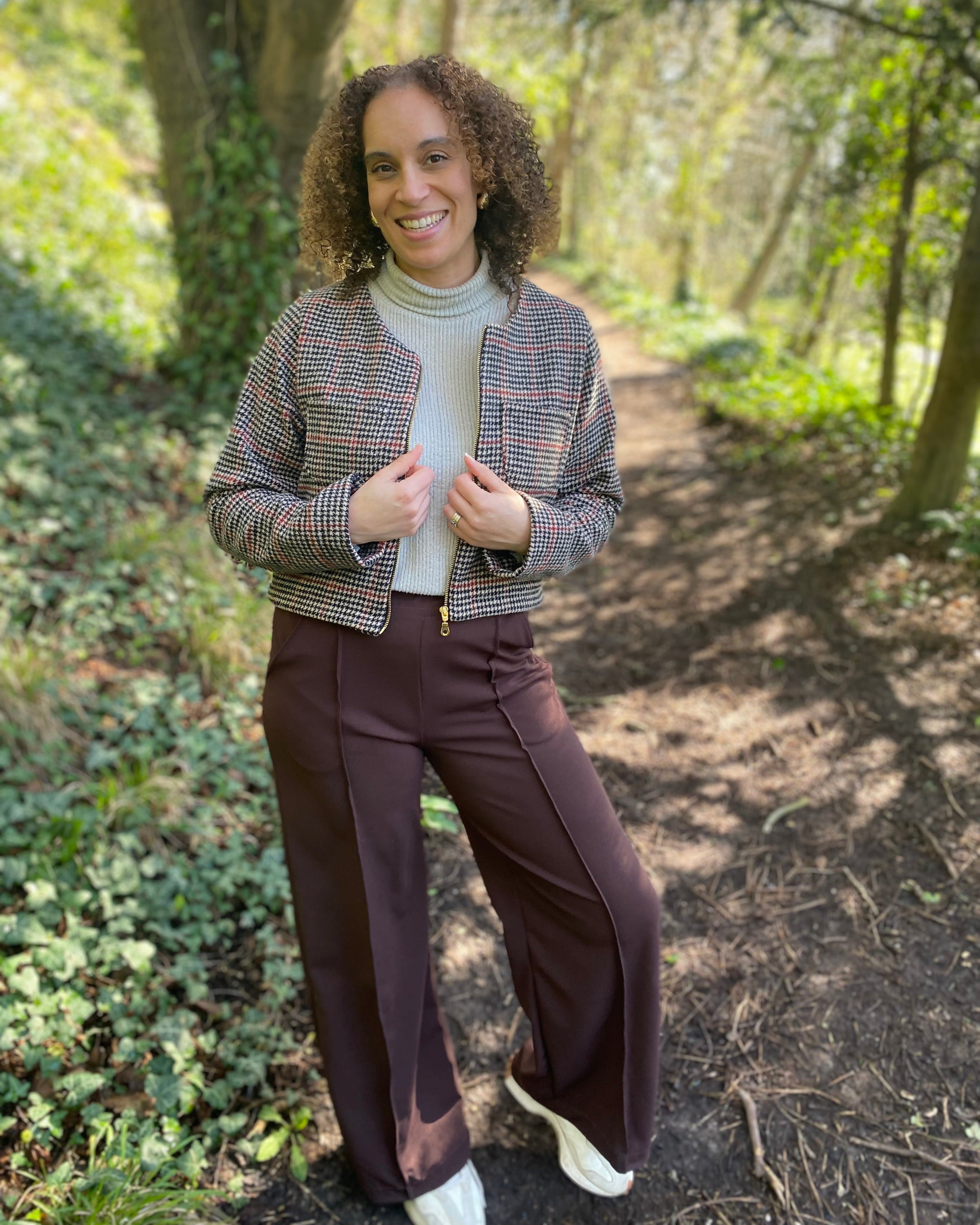 Woman standing in a forested area wearing a patterned jacket and brown pants. Made using ellie and mac PDF sewing patterns.