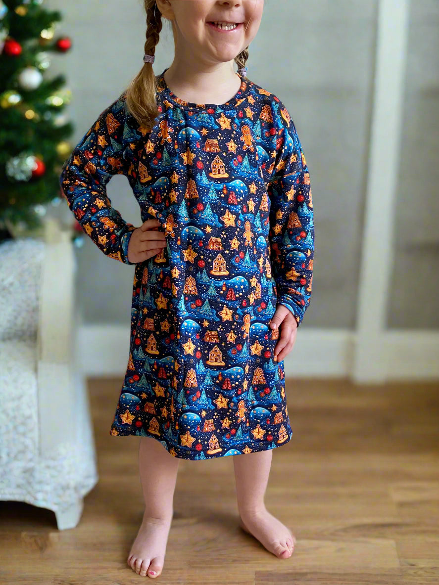 Child wearing a holiday patterned dress standing in front of a fireplace.