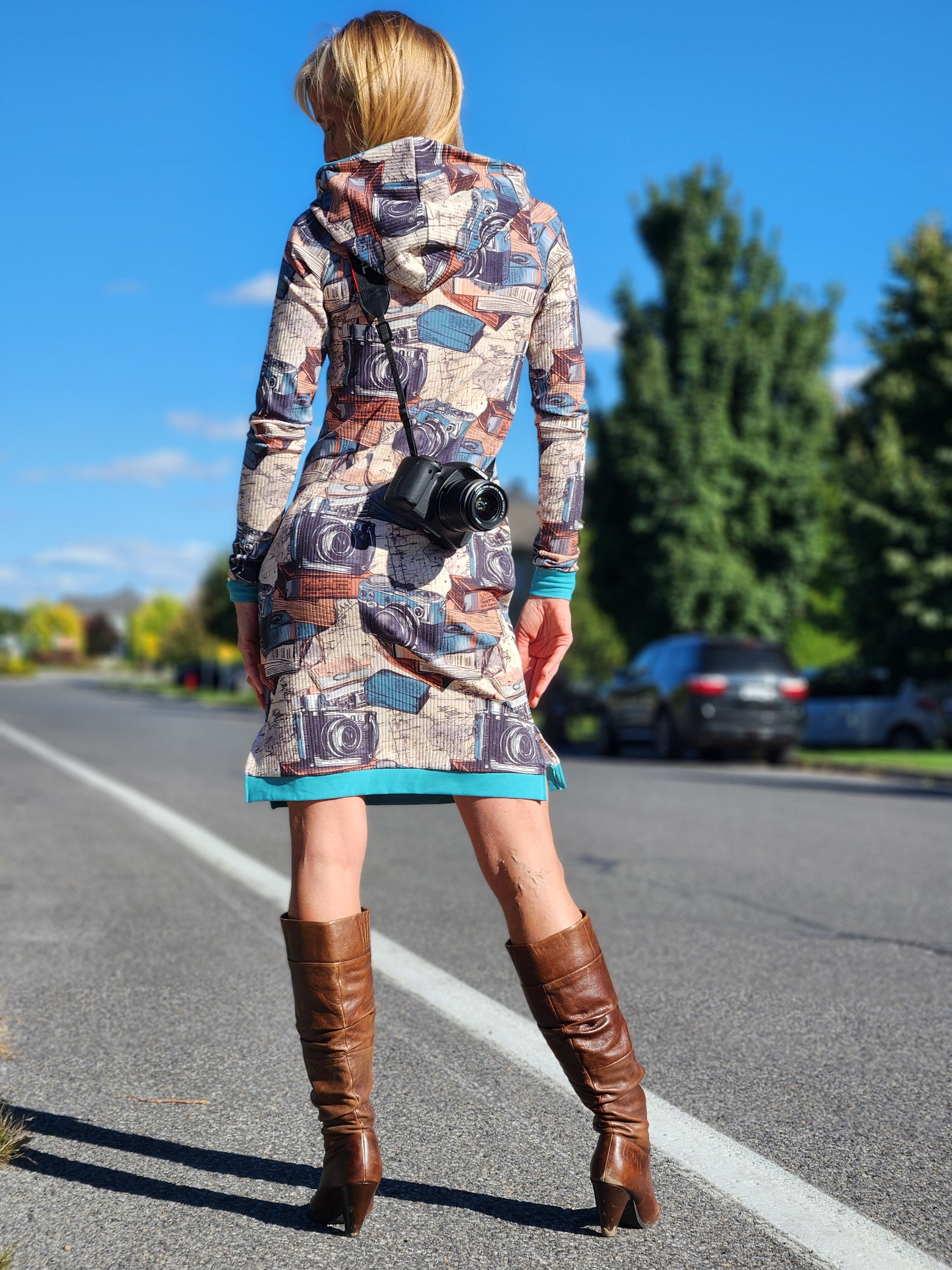 Person wearing a patterned dress and brown boots on a road with trees in the background