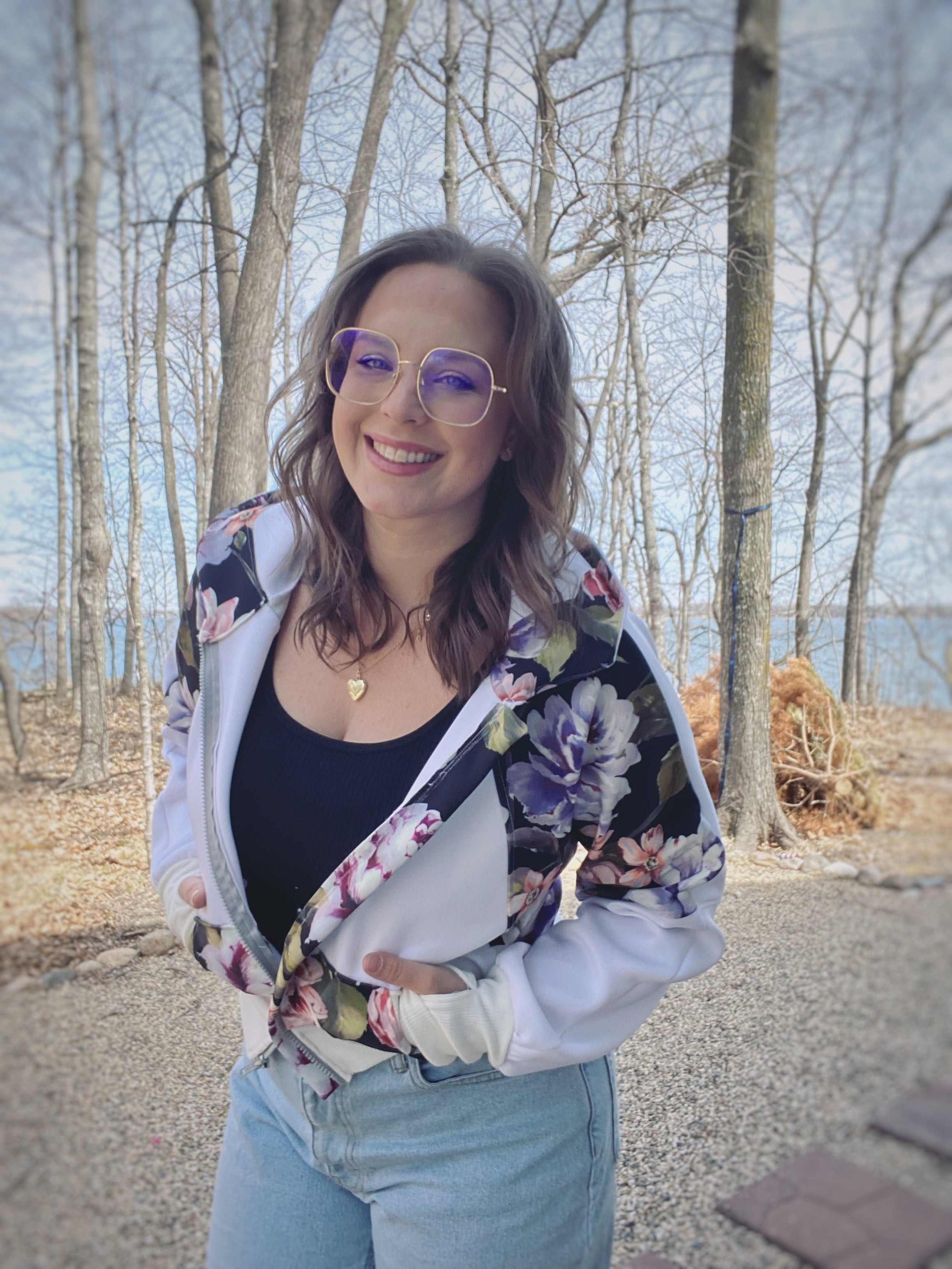 Woman outside by a lake modeling a bright color-block white and floral athletic bomber jacket with zip closure and scuba hood. Cropped version. Ellie and Mac PDF sewing patterns.