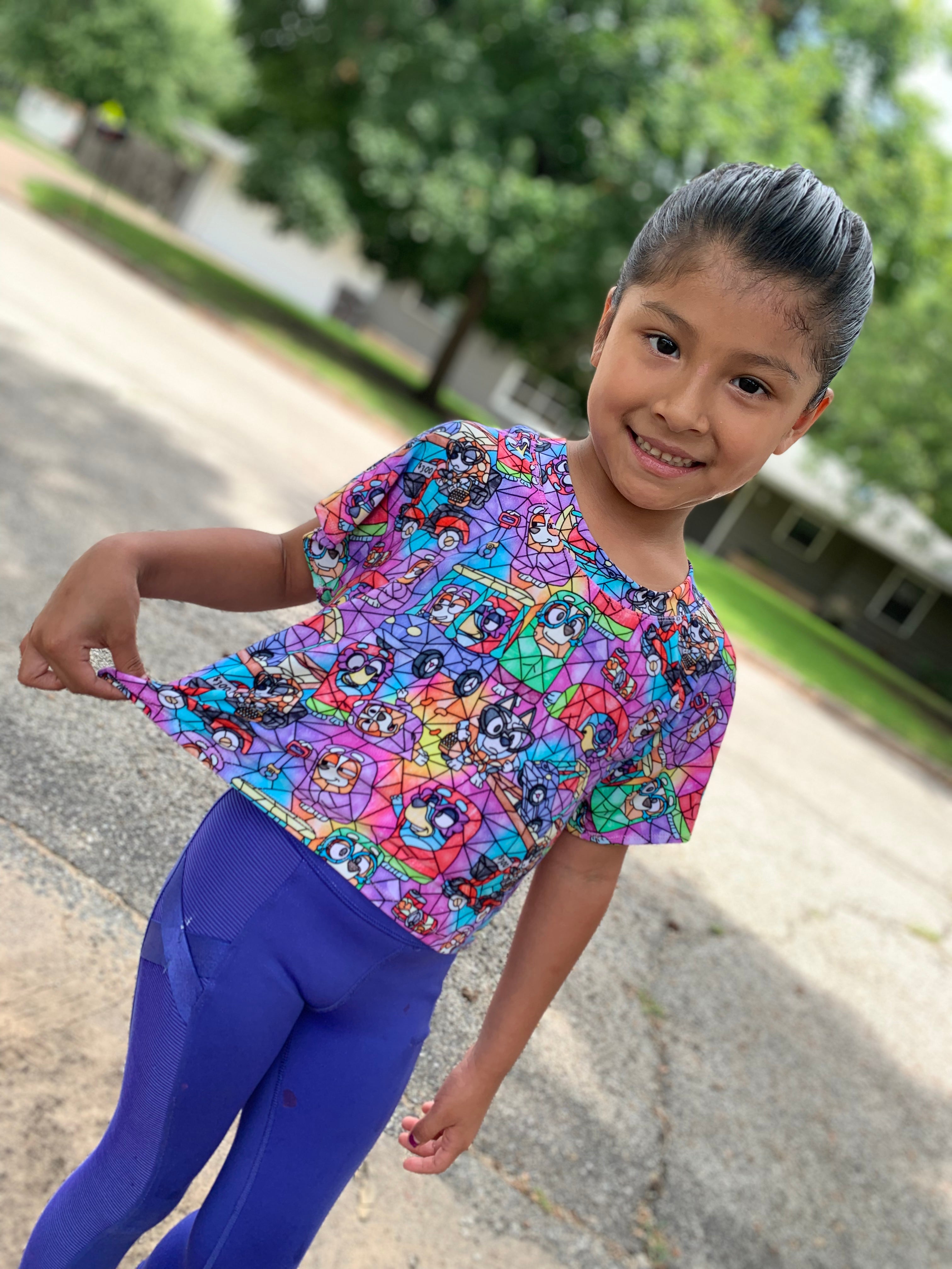 Child wearing a colorful top with floral patterns and blue pants outdoors.