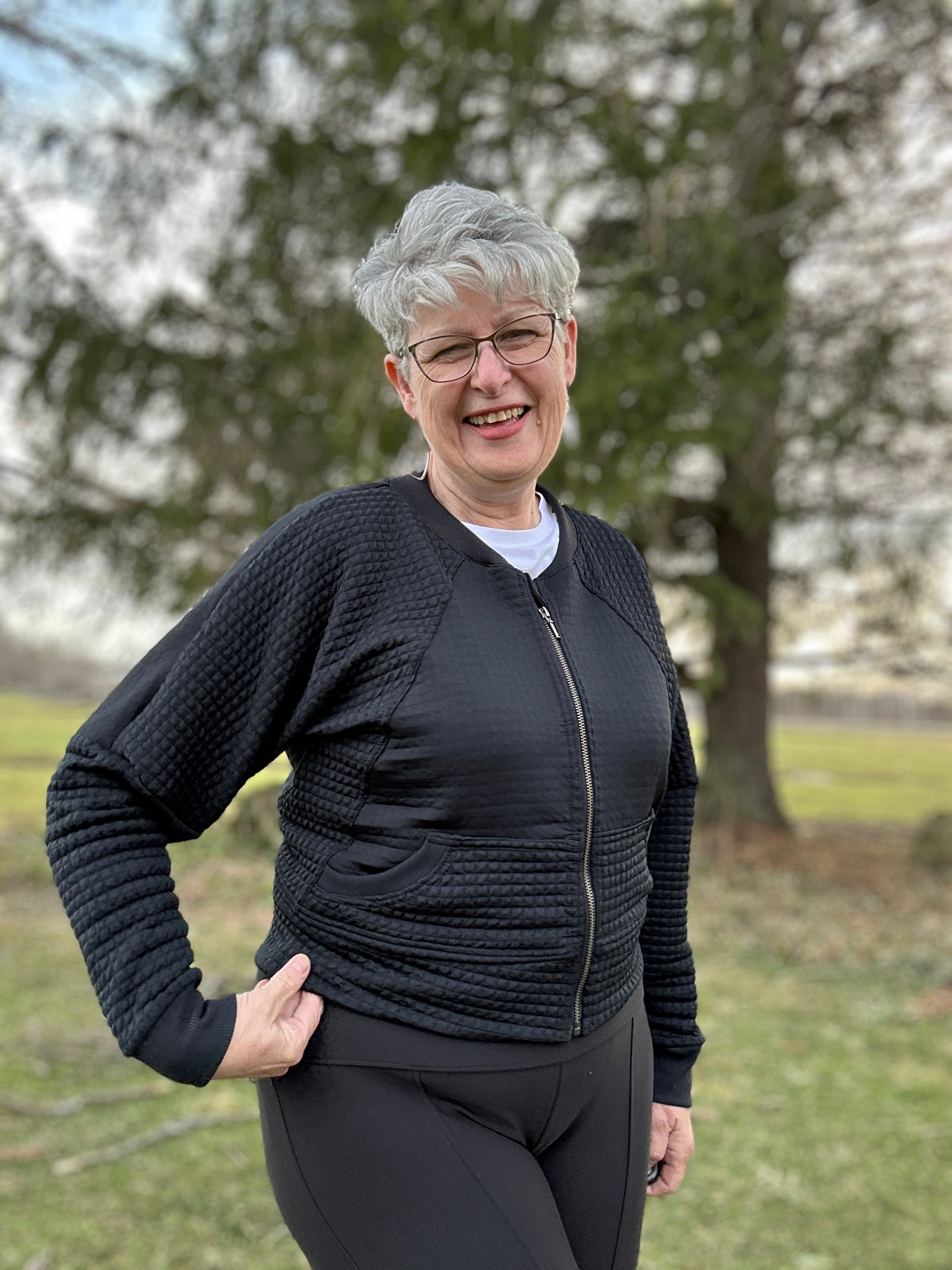 Woman outside in a park modeling a black textured fabric knit bomber jacket with zip closure. Athletic zipped closure. Ellie and Mac PDF sewing patterns.