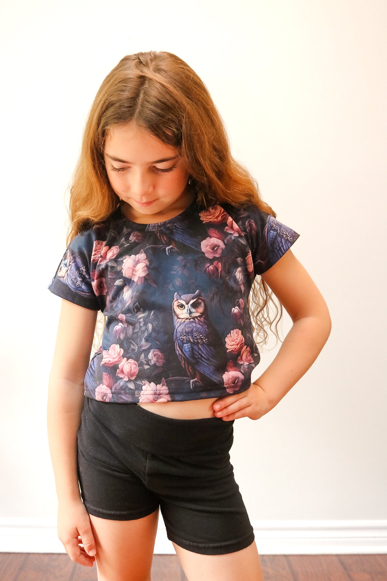 Young girl wearing a crop top with owl and floral design against a plain background