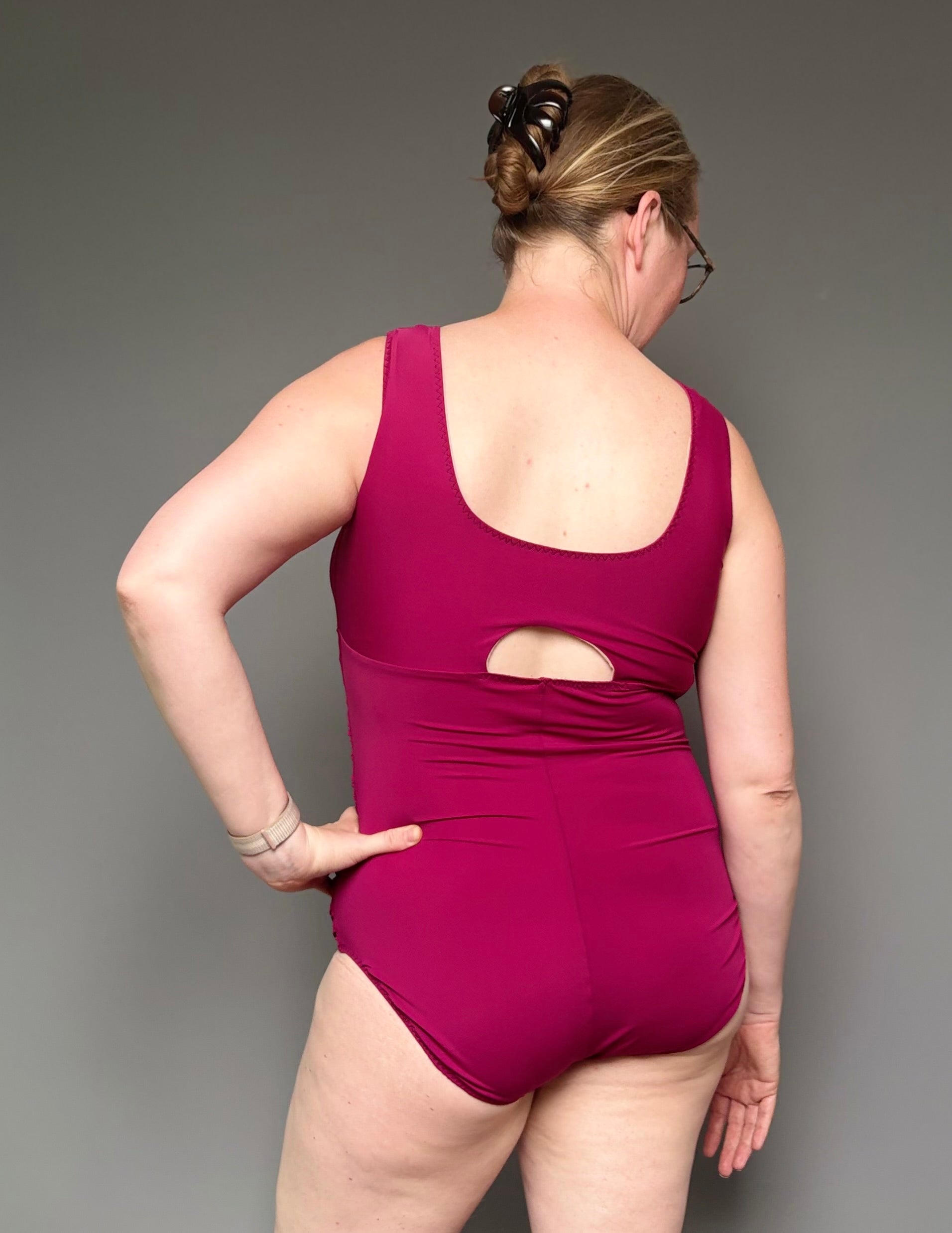Woman wearing a maroon swimsuit with cutout design on a gray background