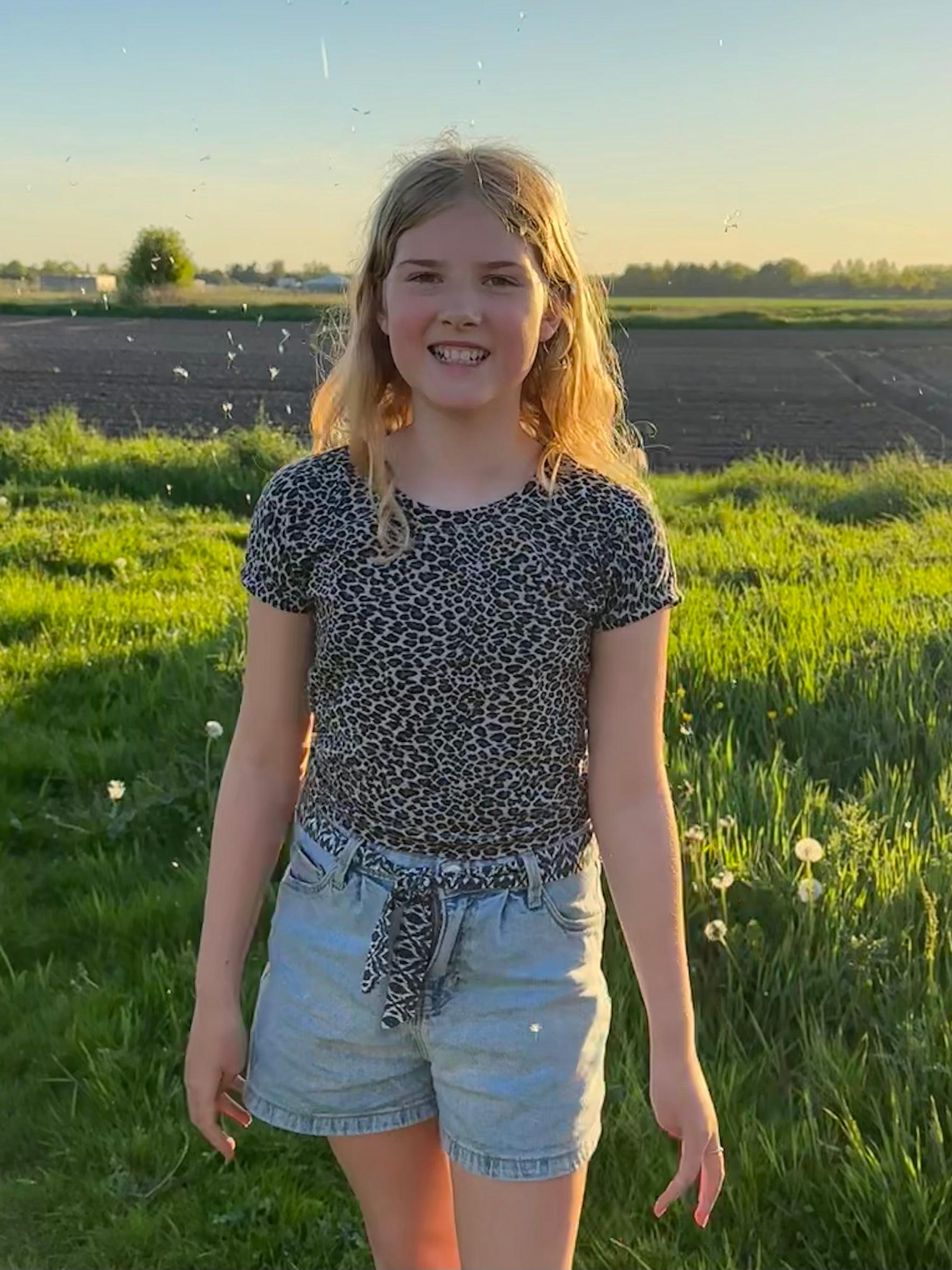 Young girl standing in a field with a scenic background wearing a cheetah print dolman top. Made using ellie and mac sewing patterns.