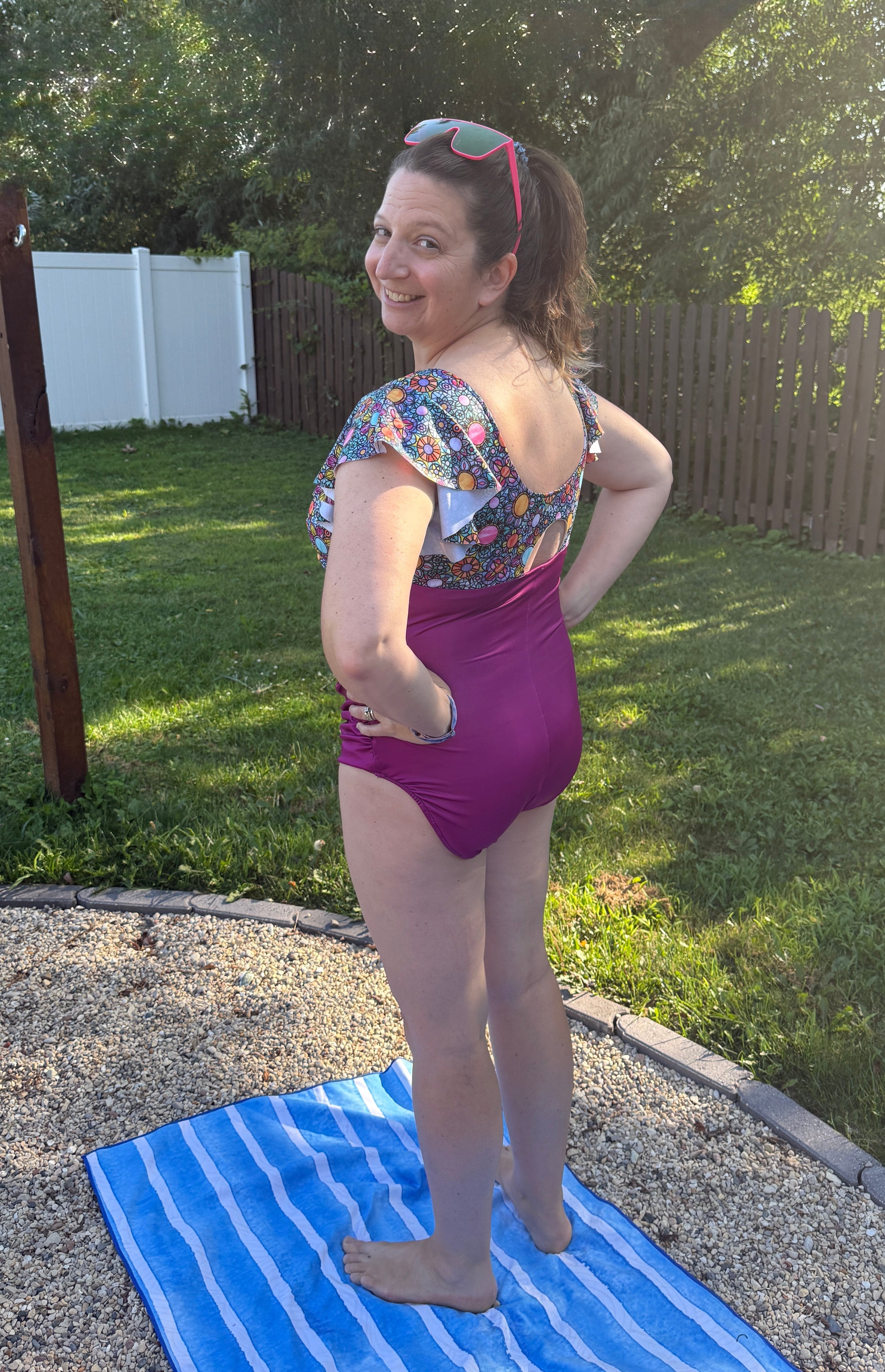 Woman in a colorful swimsuit standing on a blue towel outdoors.