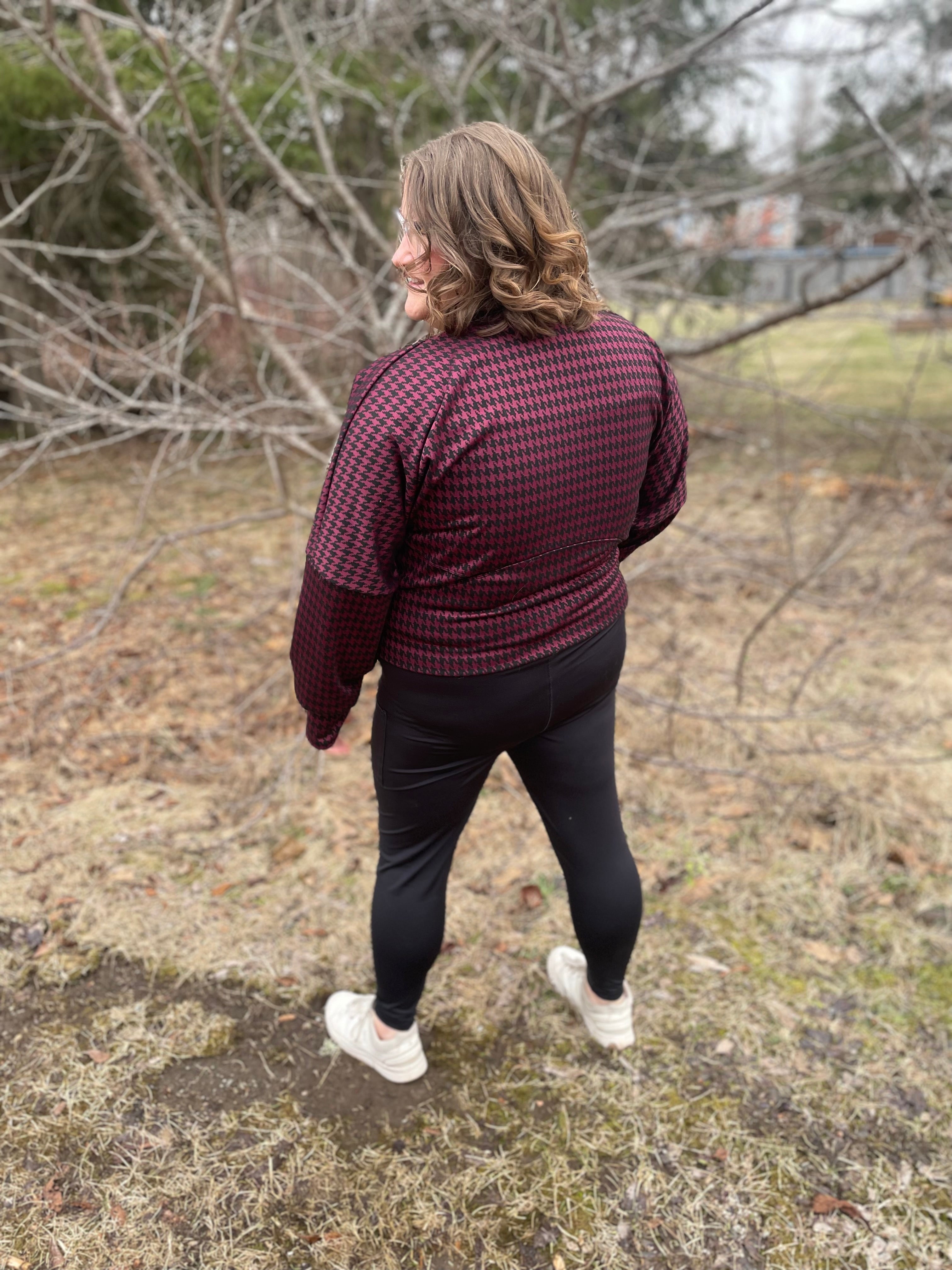 Woman outside modeling a burgundy and black houndstooth athletic bomber jacket with zip closure, kangaroo pocket detail, and thumbhole cuffs. Easy pdf sewing pattern.