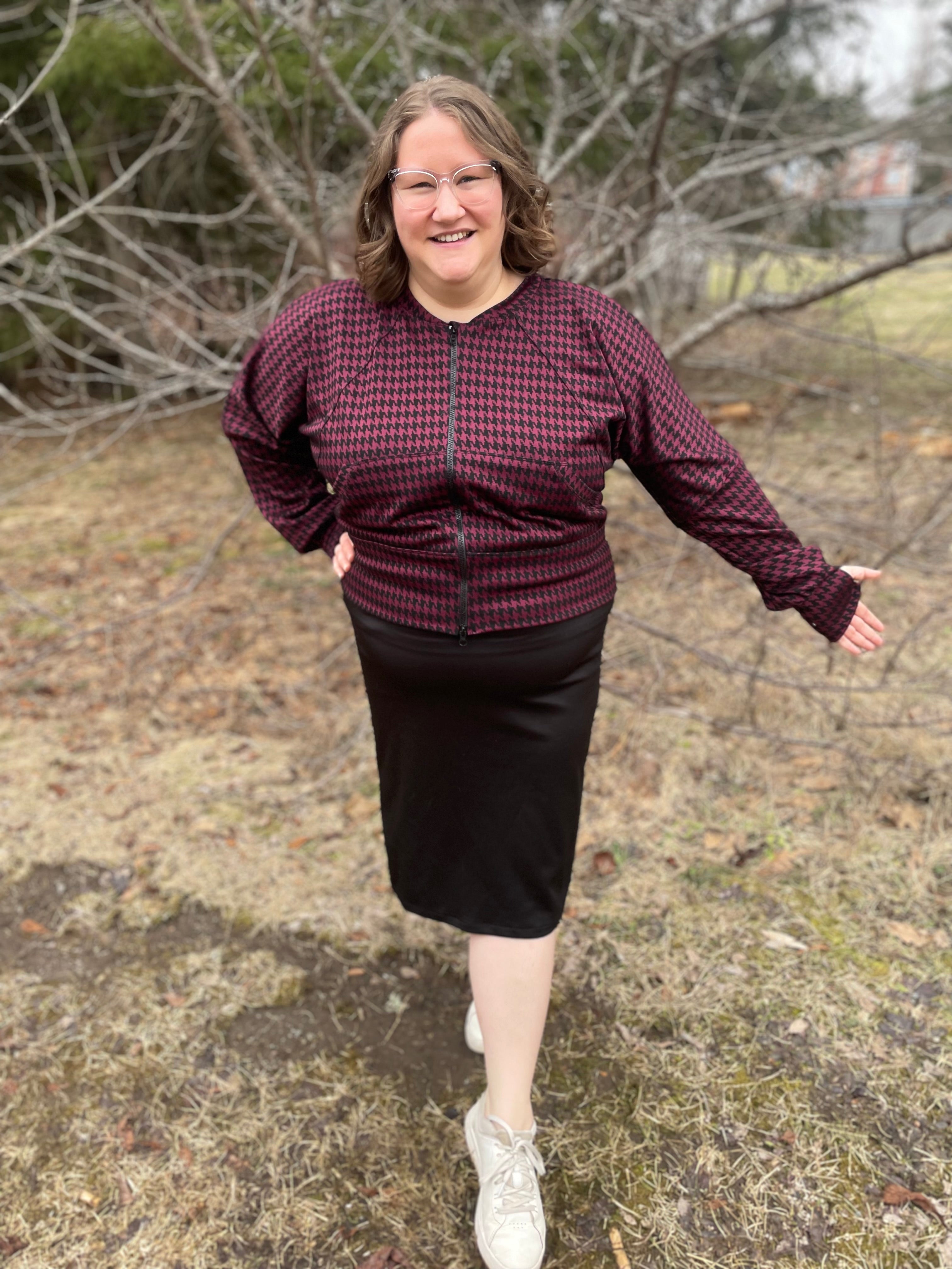 Woman outside modeling a burgundy and black houndstooth athletic bomber jacket with zip closure, kangaroo pocket detail, and thumbhole cuffs. Easy pdf sewing pattern.