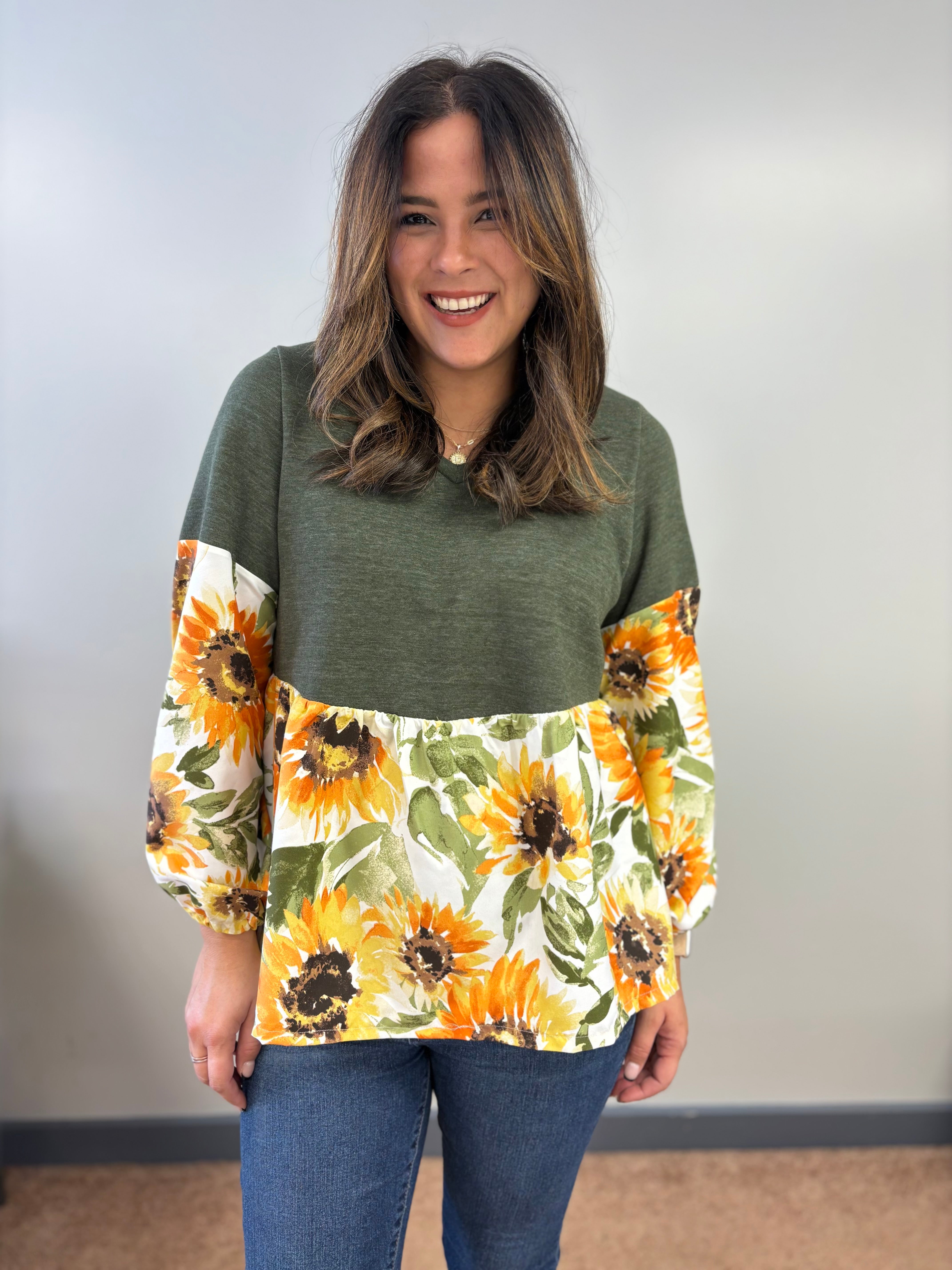 Woman wearing a green peasant sweater top with sunflower patterned sleeves and gathered skirt against a plain background