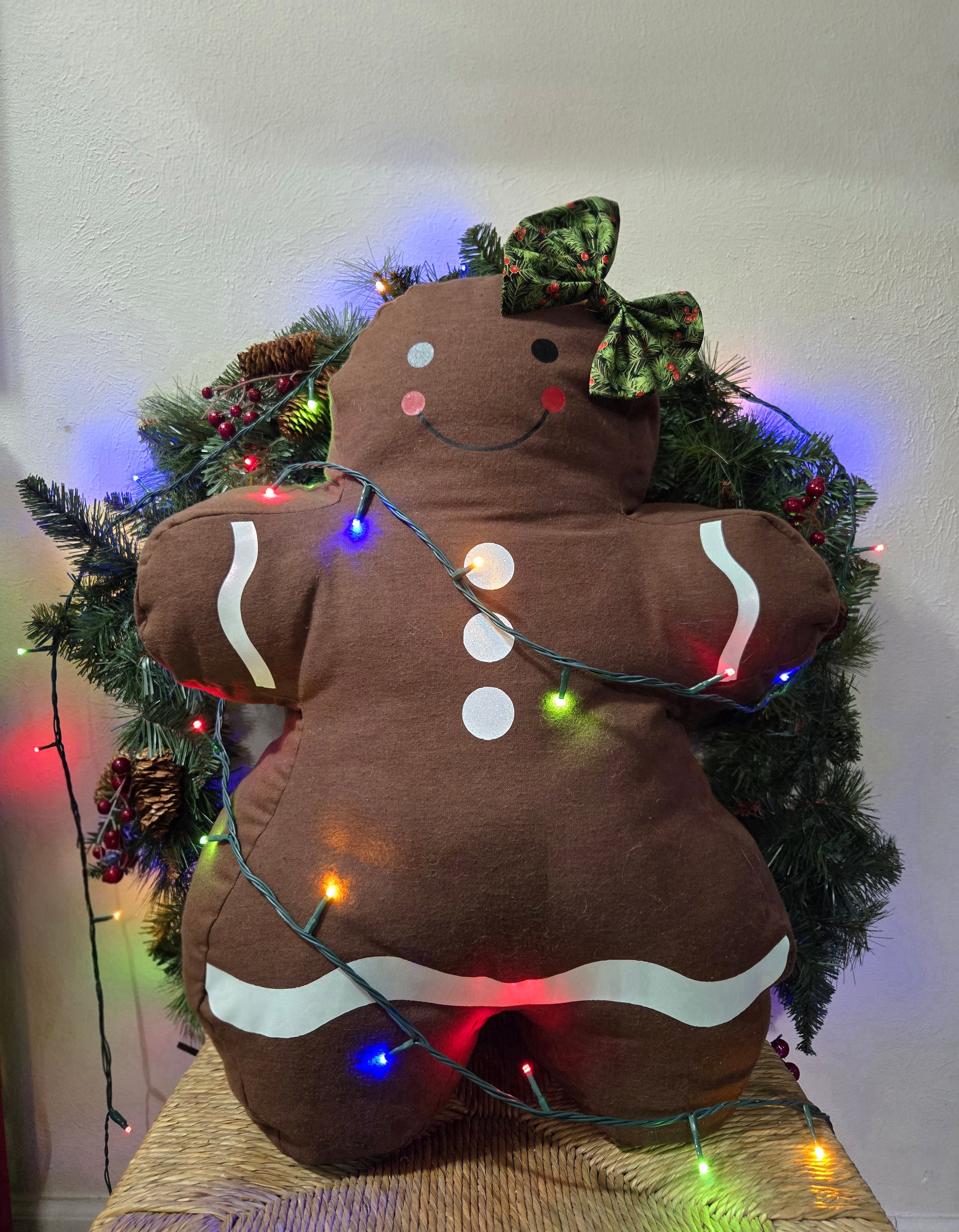Jolly Gingerbread man plush toy with string lights against a Christmas tree background