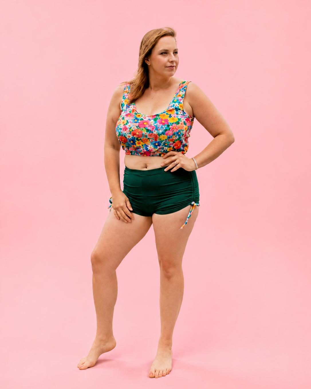 Woman wearing a colorful floral top and green shorts on a pink background. PDF sewing pattern swimwear.